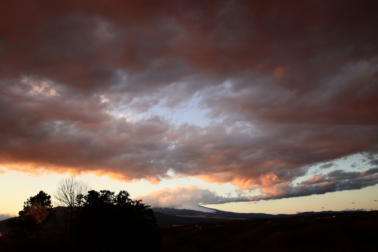 Cielo di tramonto drammatico con nuvole scure e silhouette di montagna