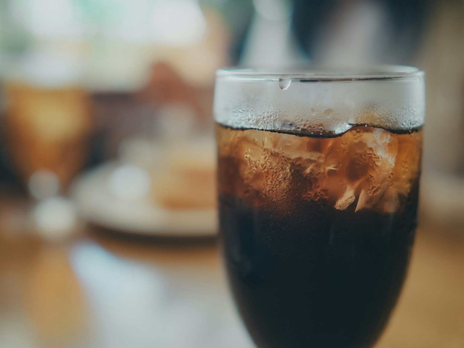 Primo piano di un bicchiere di cola con ghiaccio sfondo sfocato di bevande e cibo
