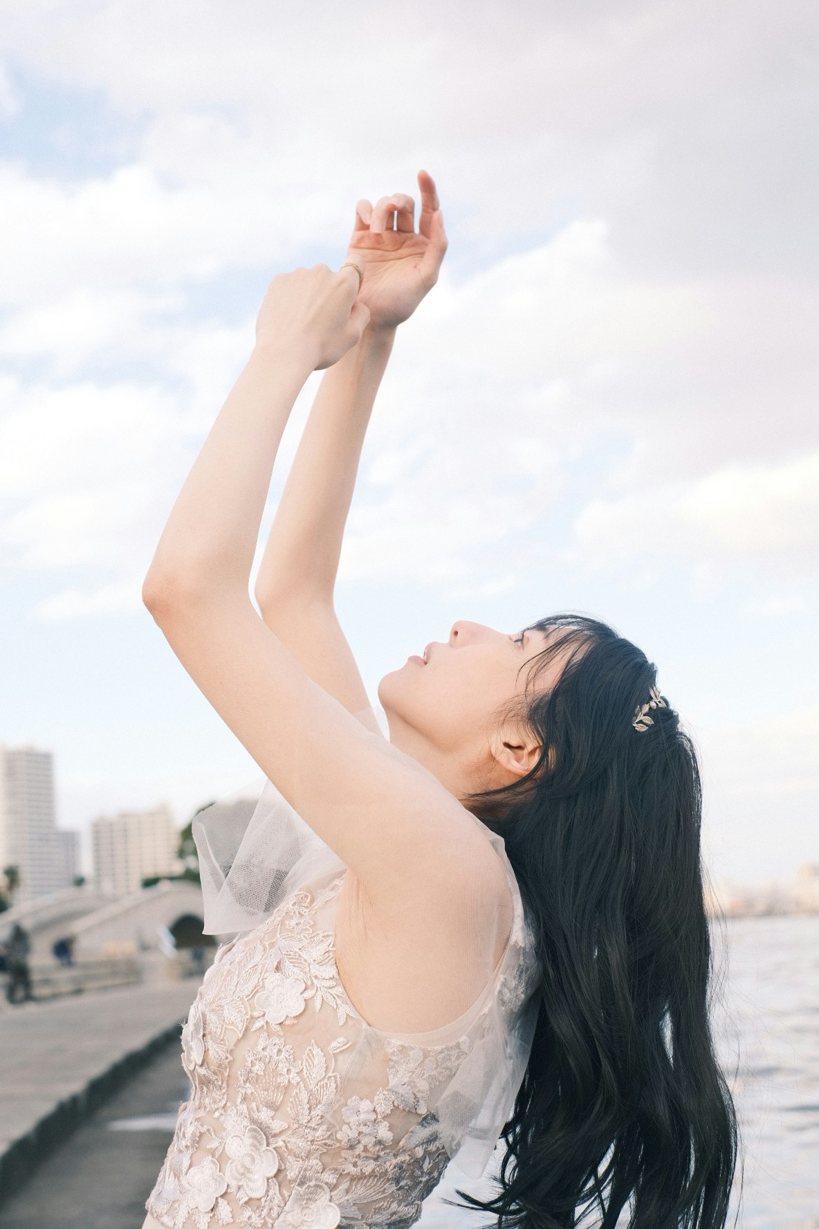 perfil de la novia levantando los brazos con skyline urbano bajo cielo nublado