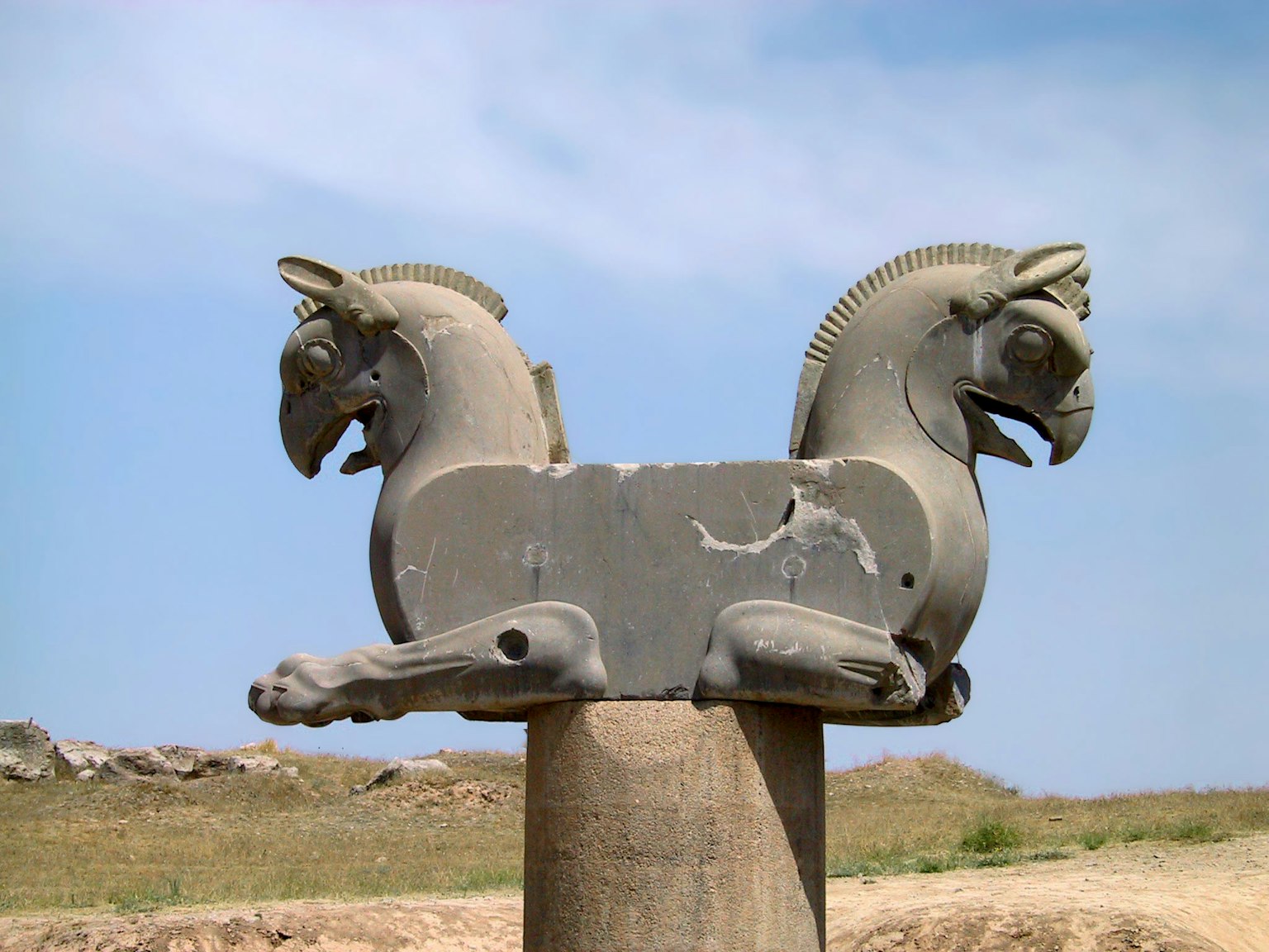 A sculpture of two horse heads on a pillar under a blue sky