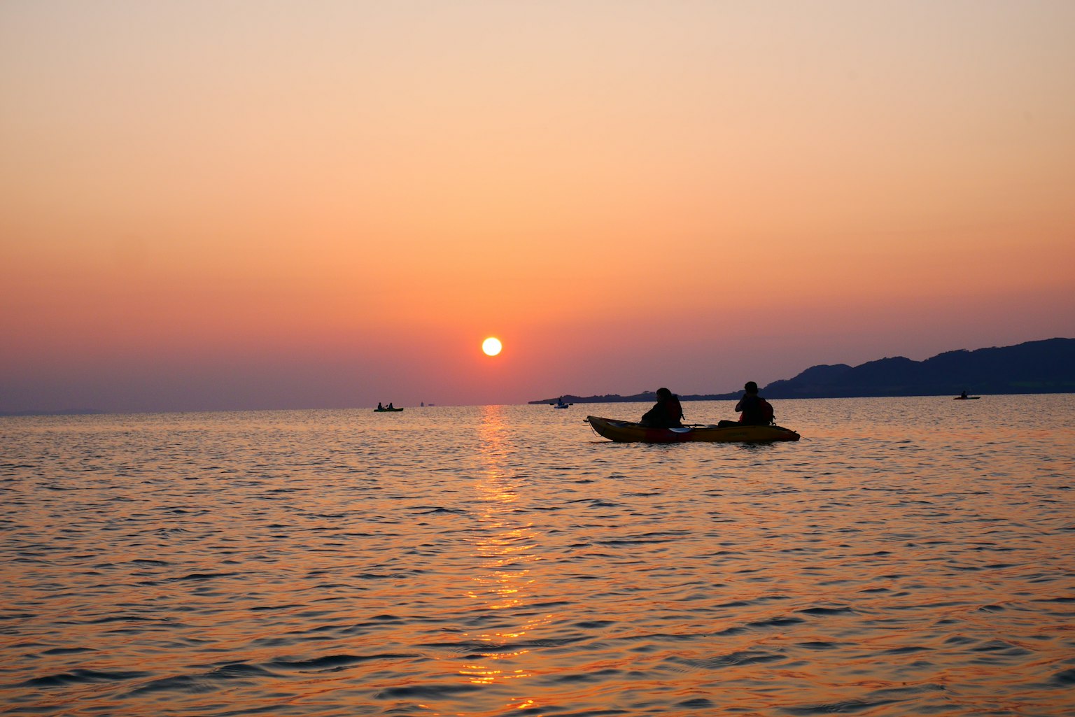Silhouette von zwei Personen beim Kajakfahren auf dem Meer bei Sonnenuntergang