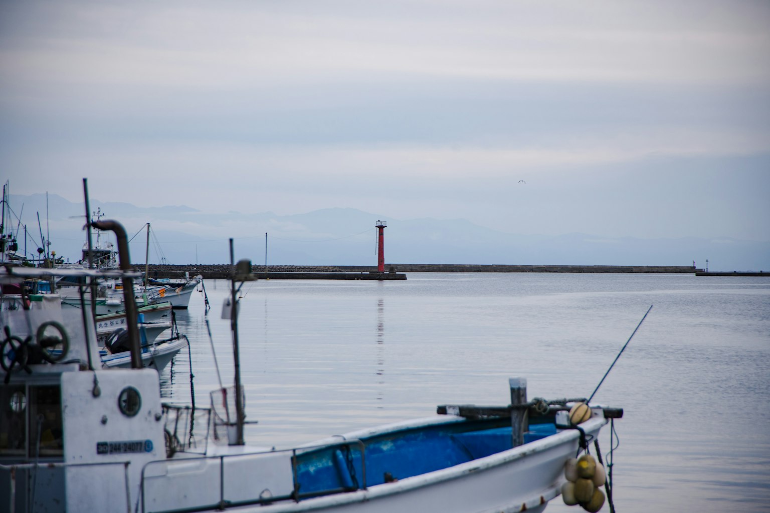 Fischerboot im ruhigen Hafen mit einem fernstehenden roten Leuchtturm