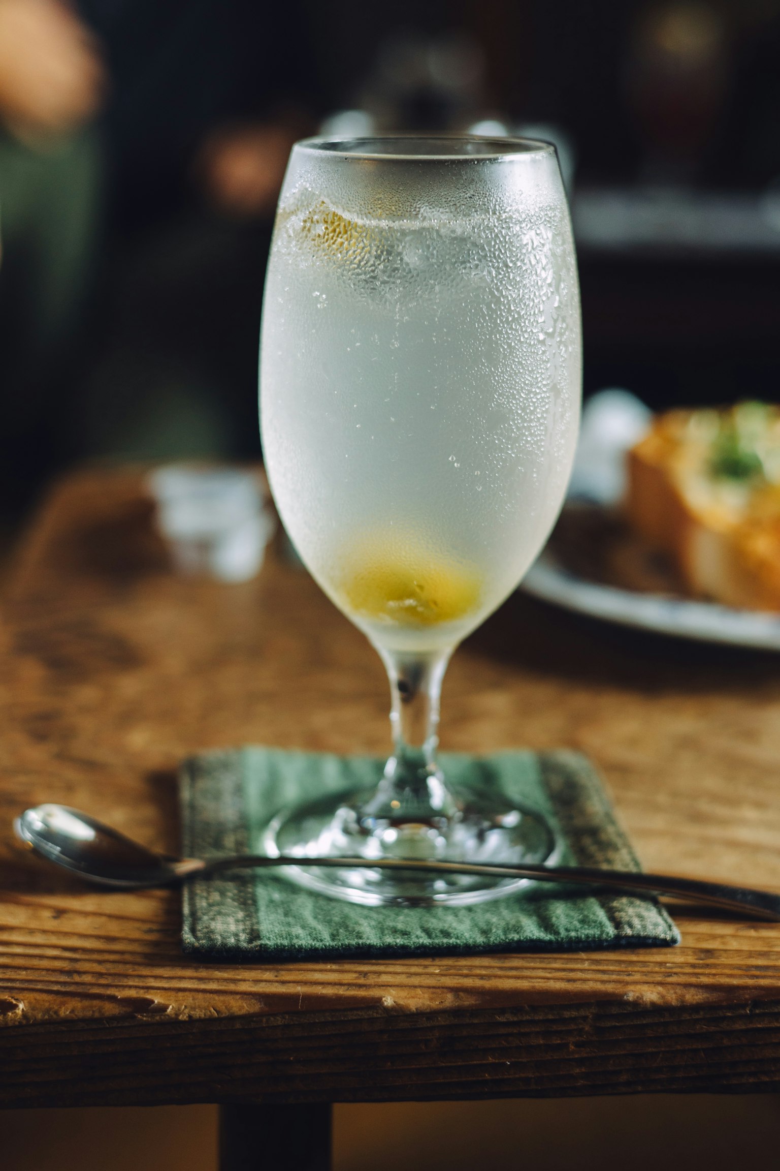 Un verre de boisson claire sur une table en bois avec un sous-verre vert