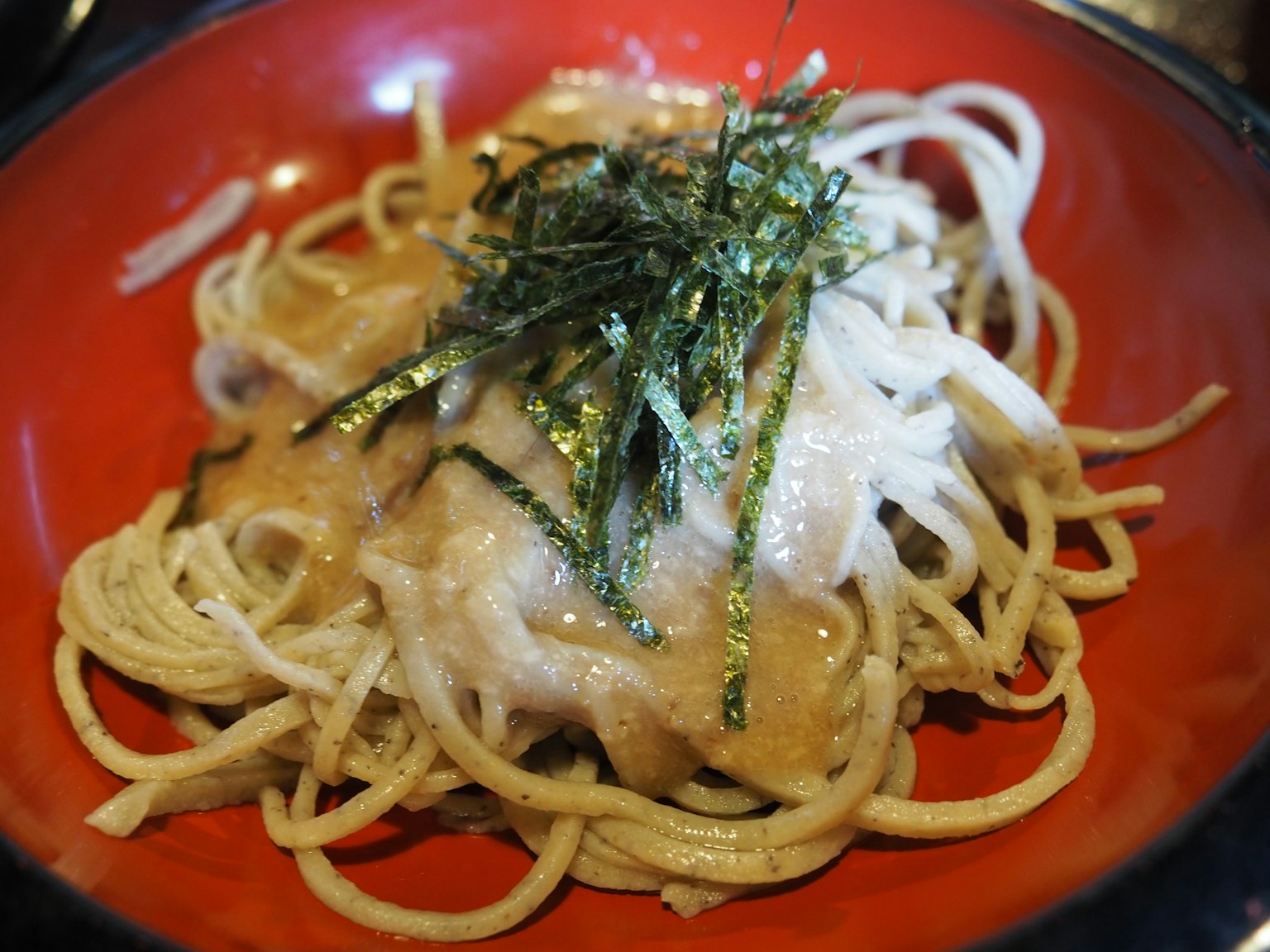 Noodles sottili serviti in una ciotola rossa guarniti con alga