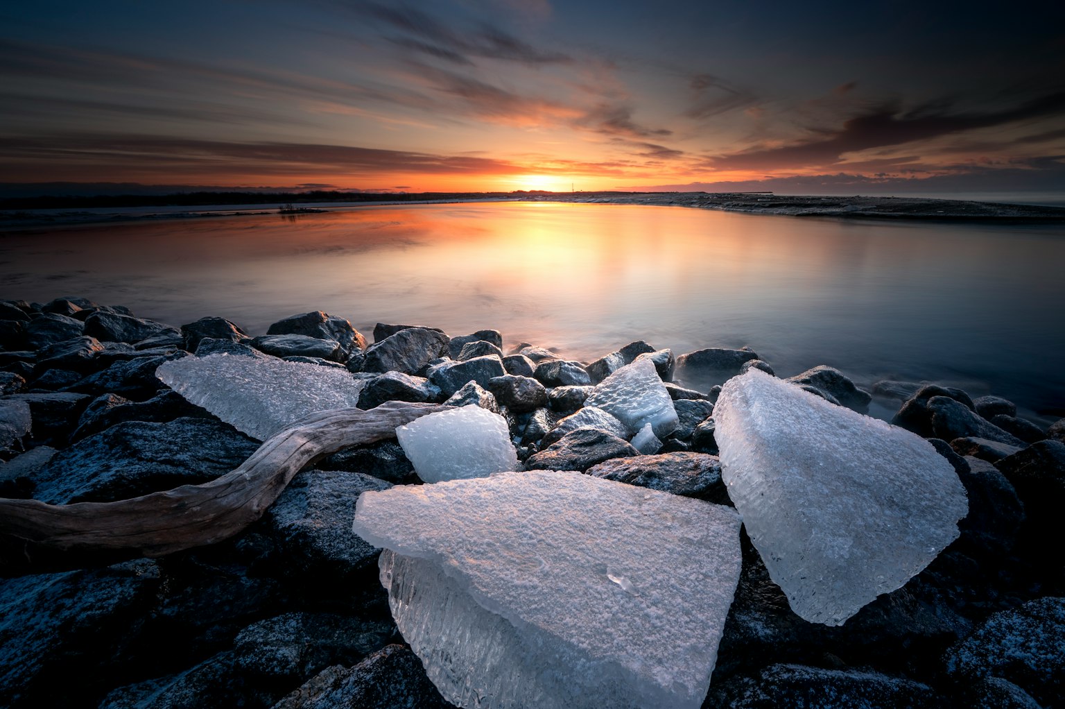 Ruhiges Wasser, das den Sonnenuntergang mit Steinen am Ufer spiegelt