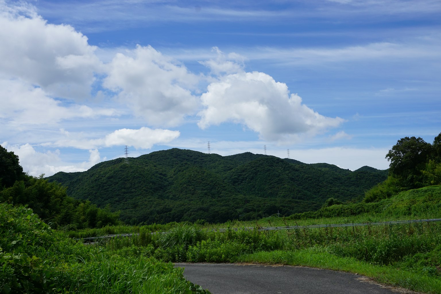 Scenic view of a green mountain under a blue sky with white clouds and a road