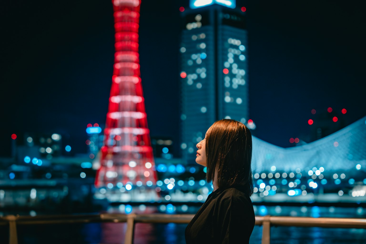夜景の中で横向きの女性と赤いタワー