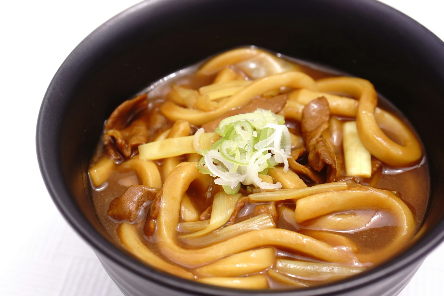 Fideos udon calientes en un tazón negro cubiertos con cebollas verdes y caldo sabroso