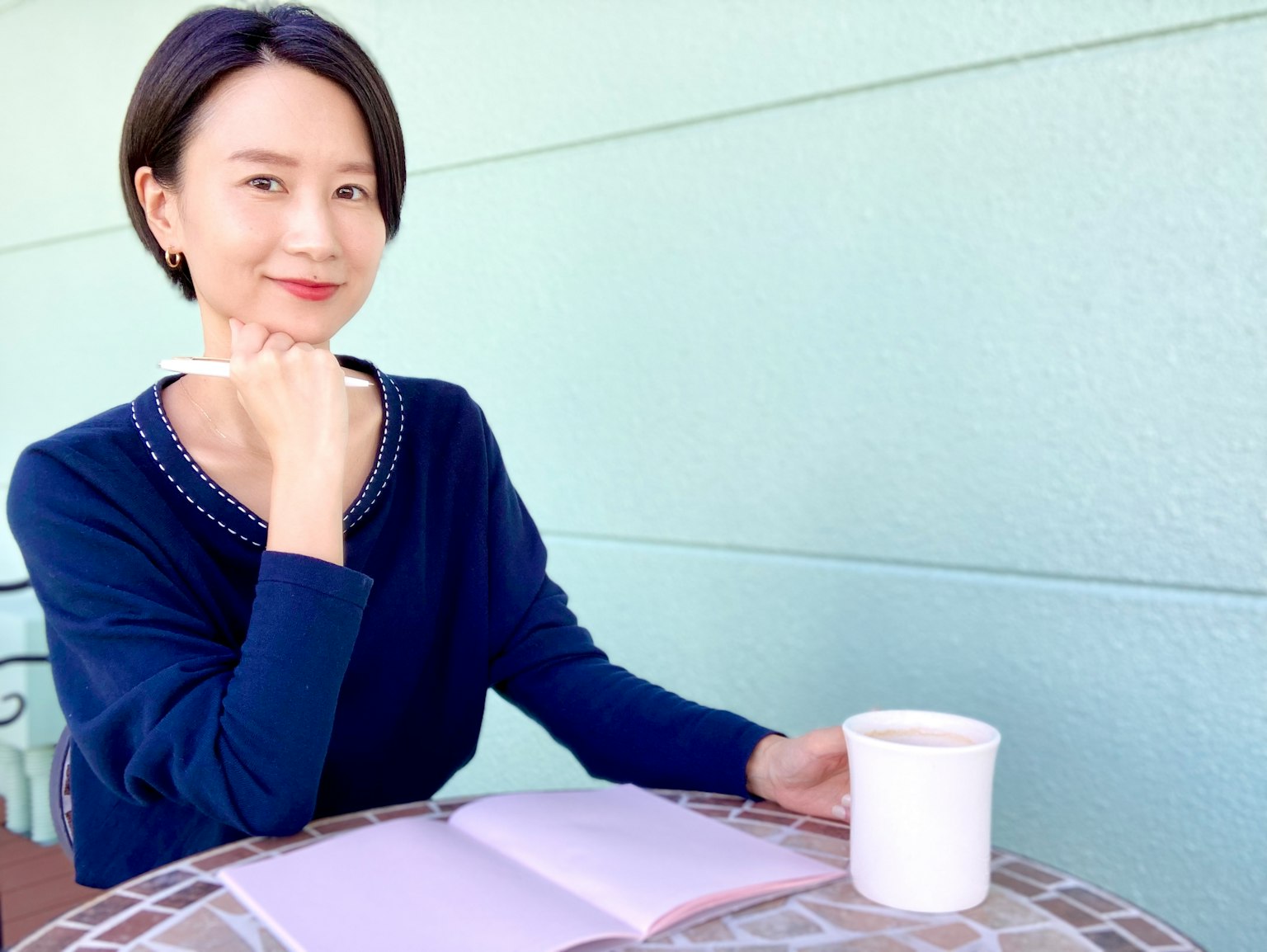 Một người phụ nữ trong áo len màu xanh ngồi tại bàn cà phê cầm cốc cà phê