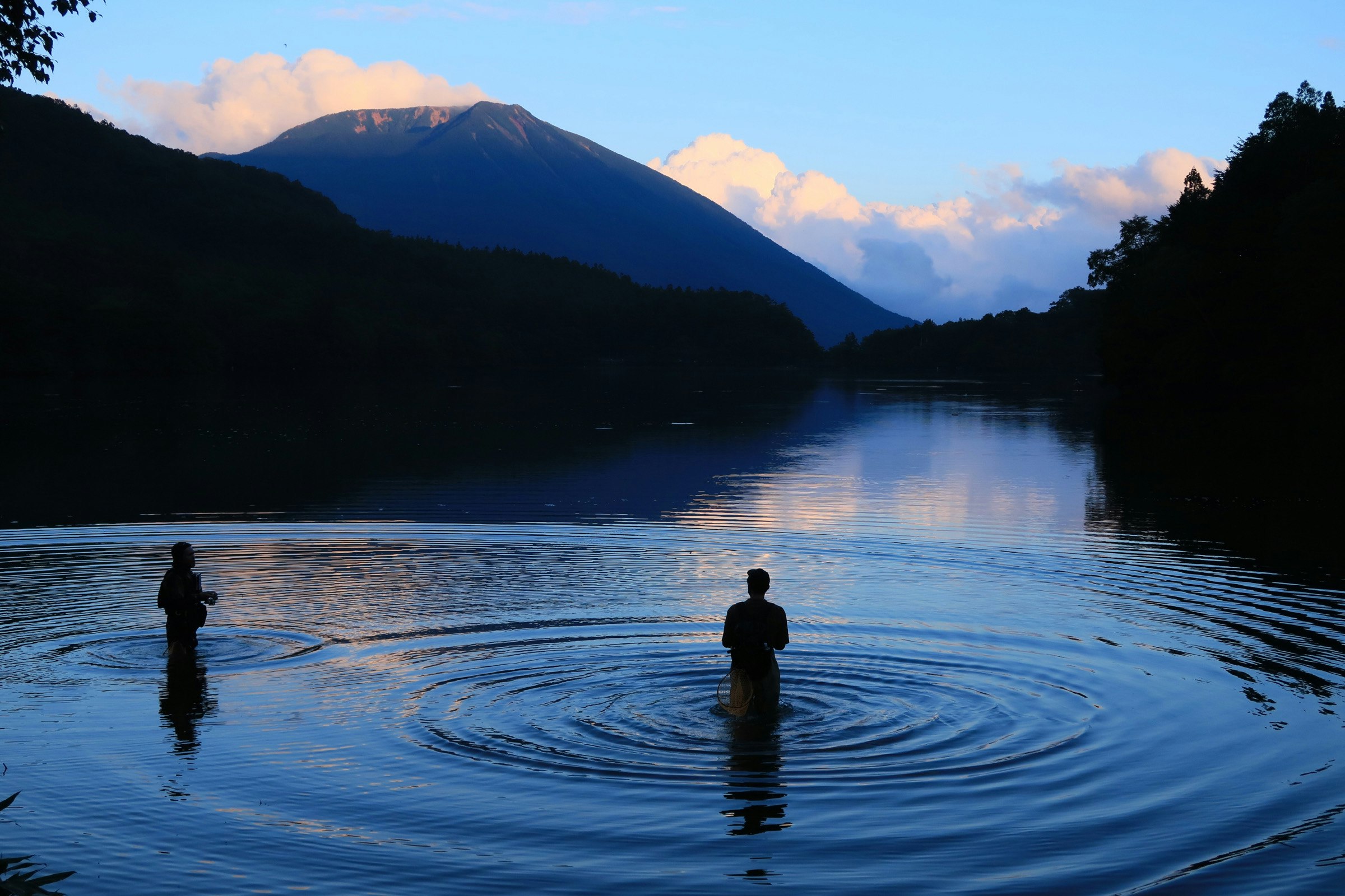 People fishing at Lake Yunoko at summer dusk with calm water and mountains in Oku-Nikko