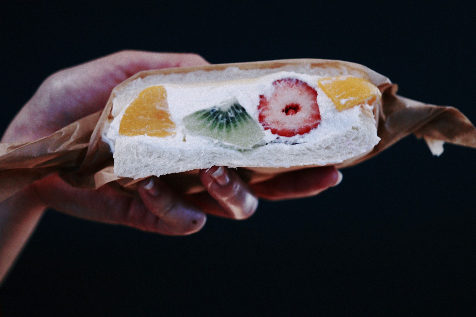 Potongan melintang sandwich buah yang dipegang di tangan menunjukkan buah berwarna-warni