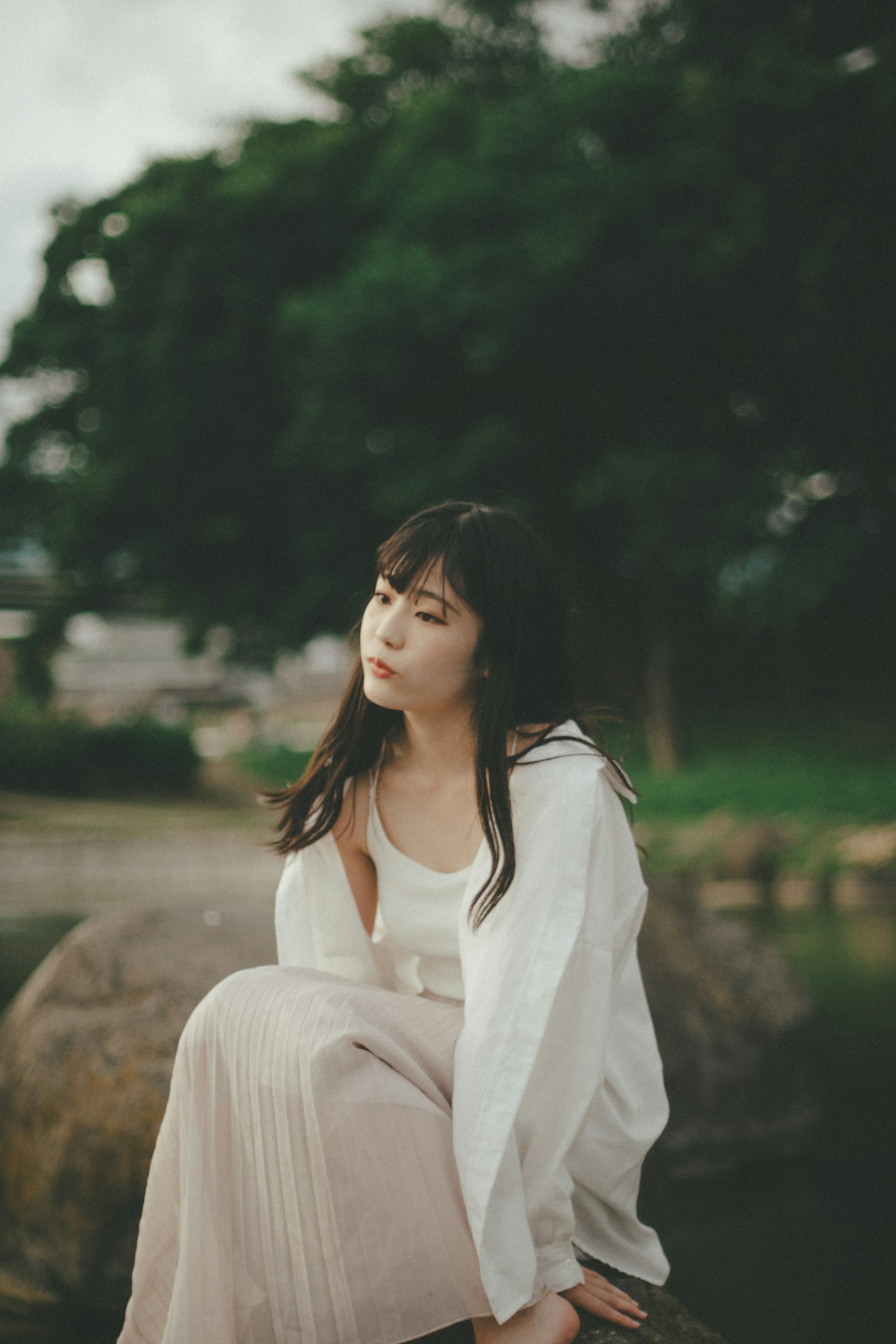 一位穿着白色衣服的女性坐在宁静公园的岩石上