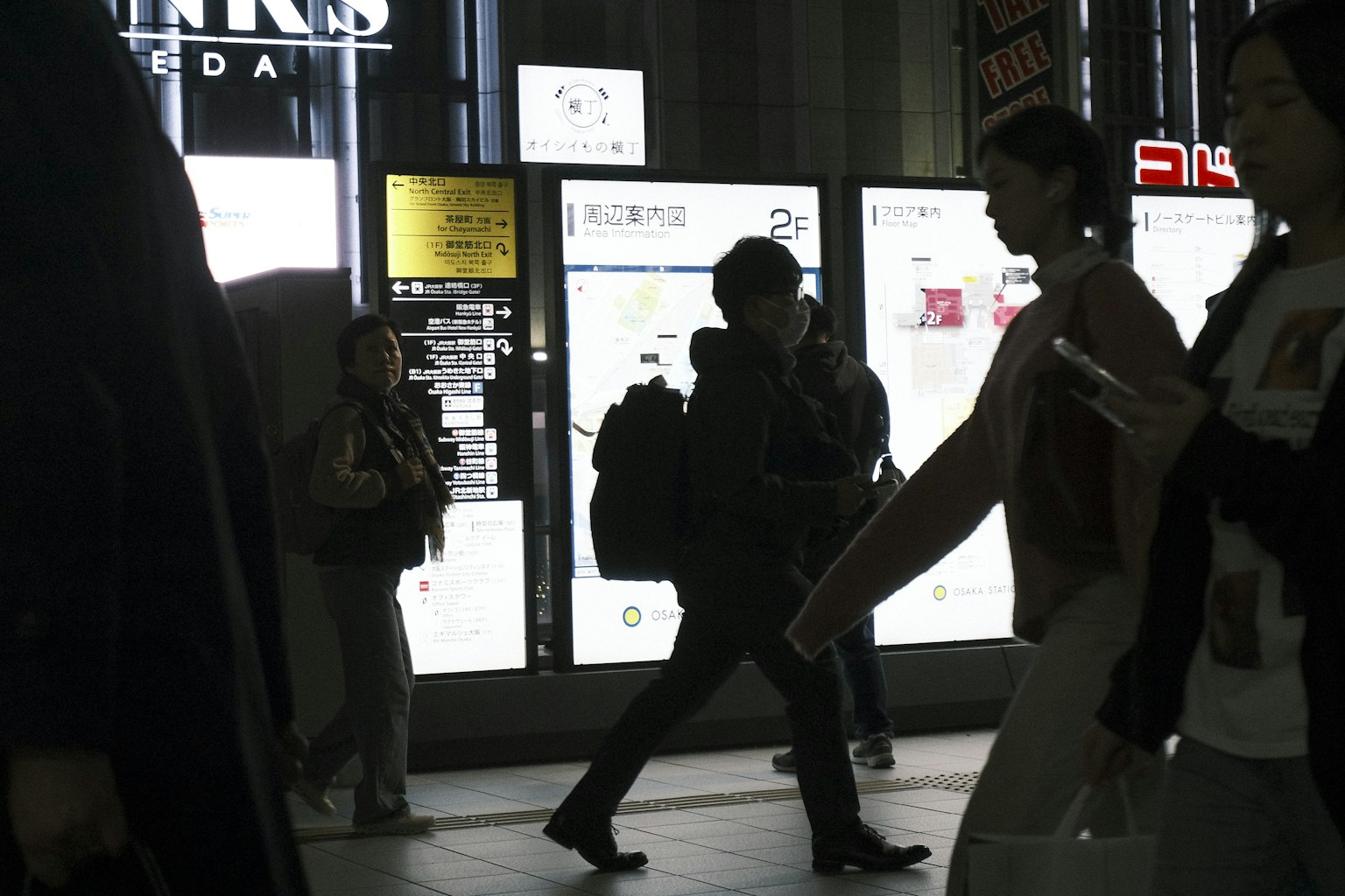 Scena urbana buia con persone che camminano e insegne luminose