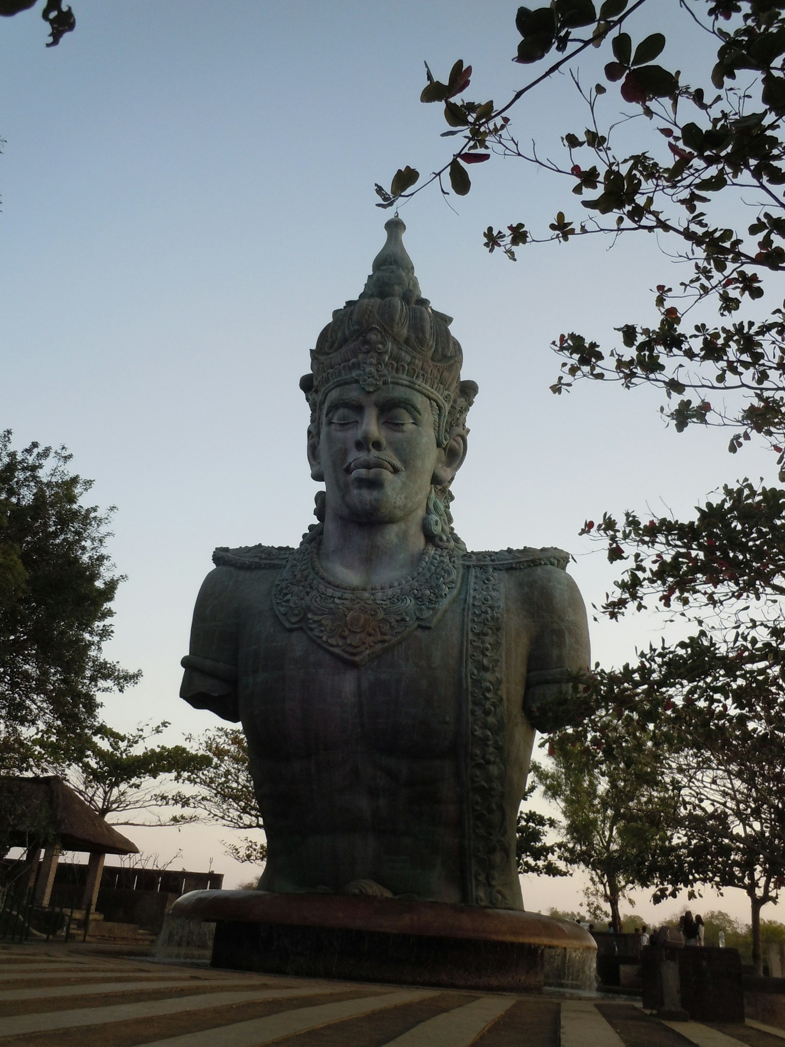 Large bust of a Buddha statue standing at dusk surrounded by trees creating a serene atmosphere