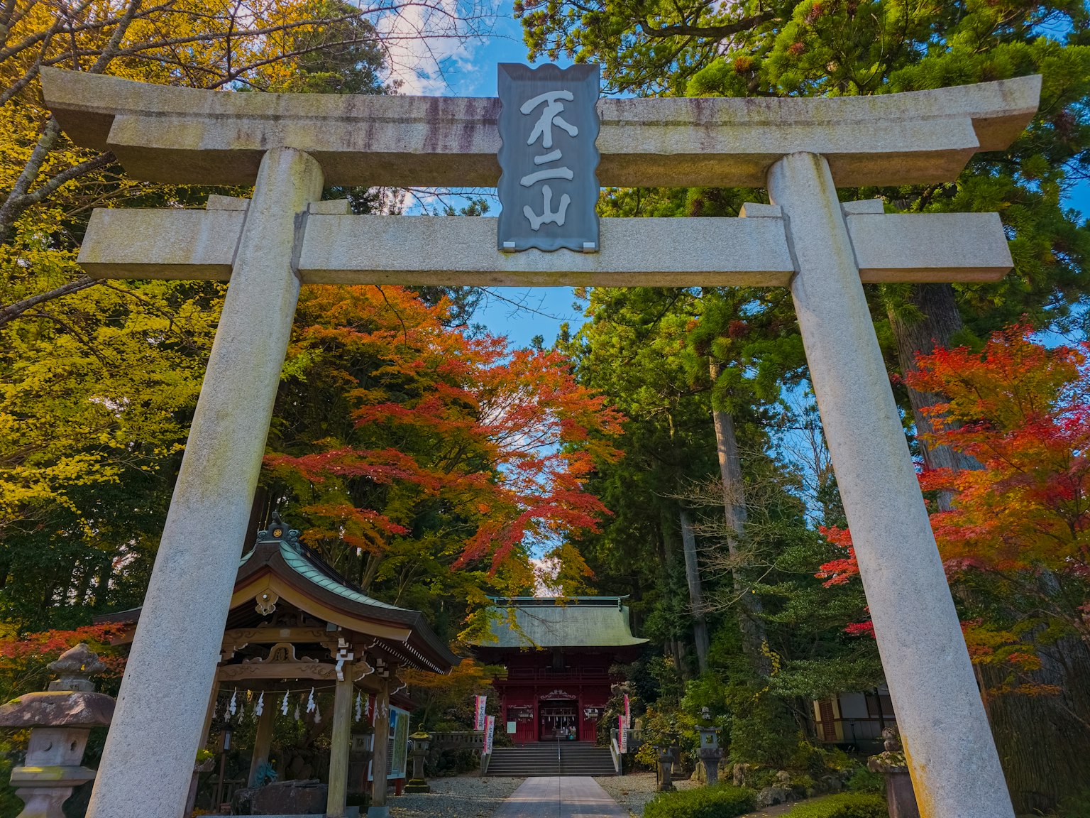 Eingang eines Schreins mit einem Torii, umgeben von lebhaftem Herbstlaub