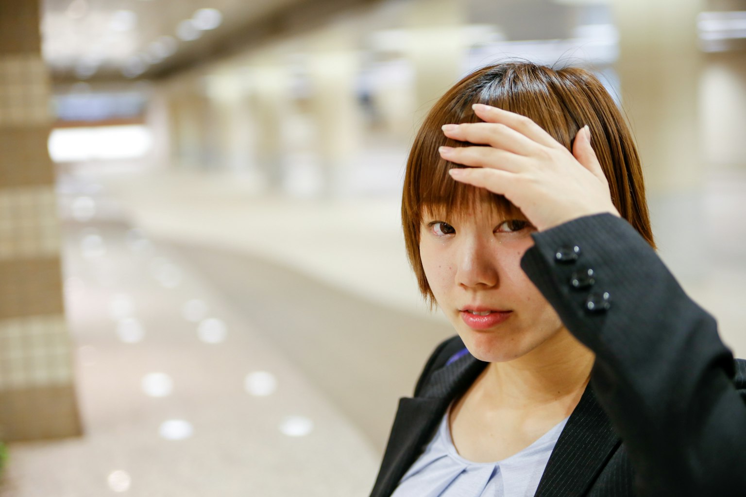 Woman in business attire touching her forehead in a modern interior