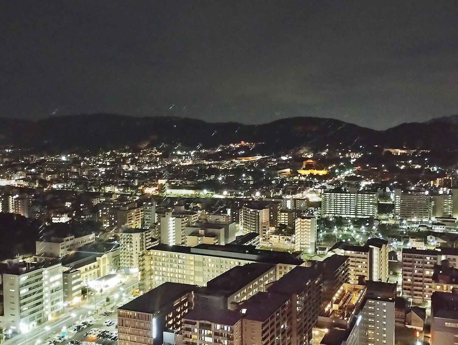 Night cityscape featuring high-rise buildings and mountains