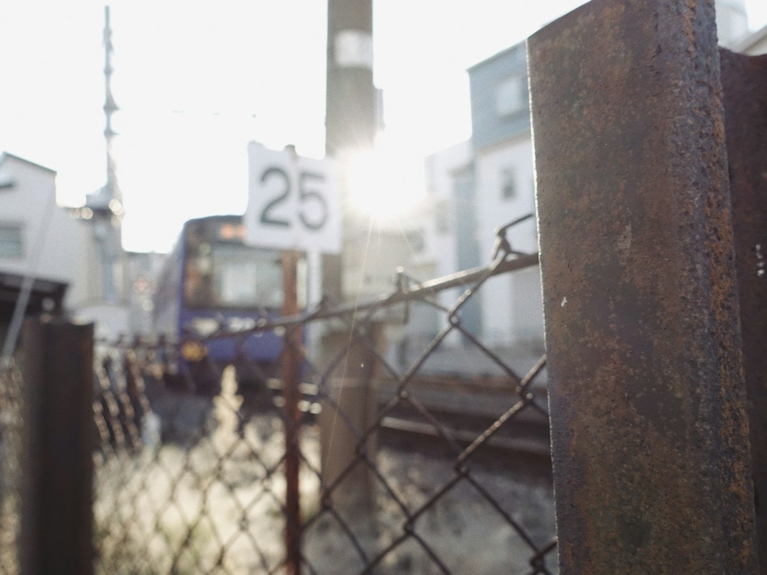 鉄道の線路とフェンスがある風景に、25番の標識と列車が見える