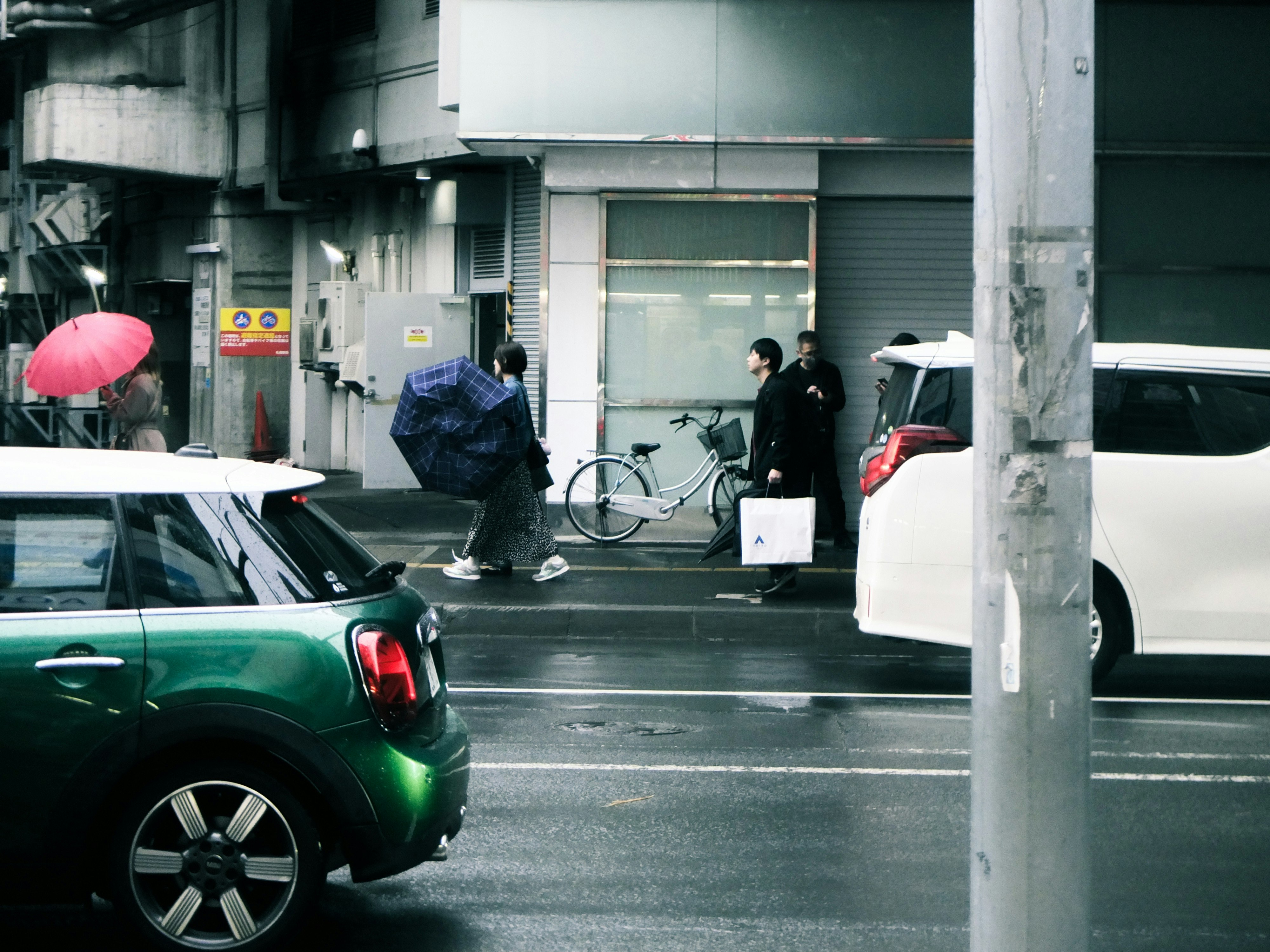 雨の路地で傘と車が並ぶ街角
