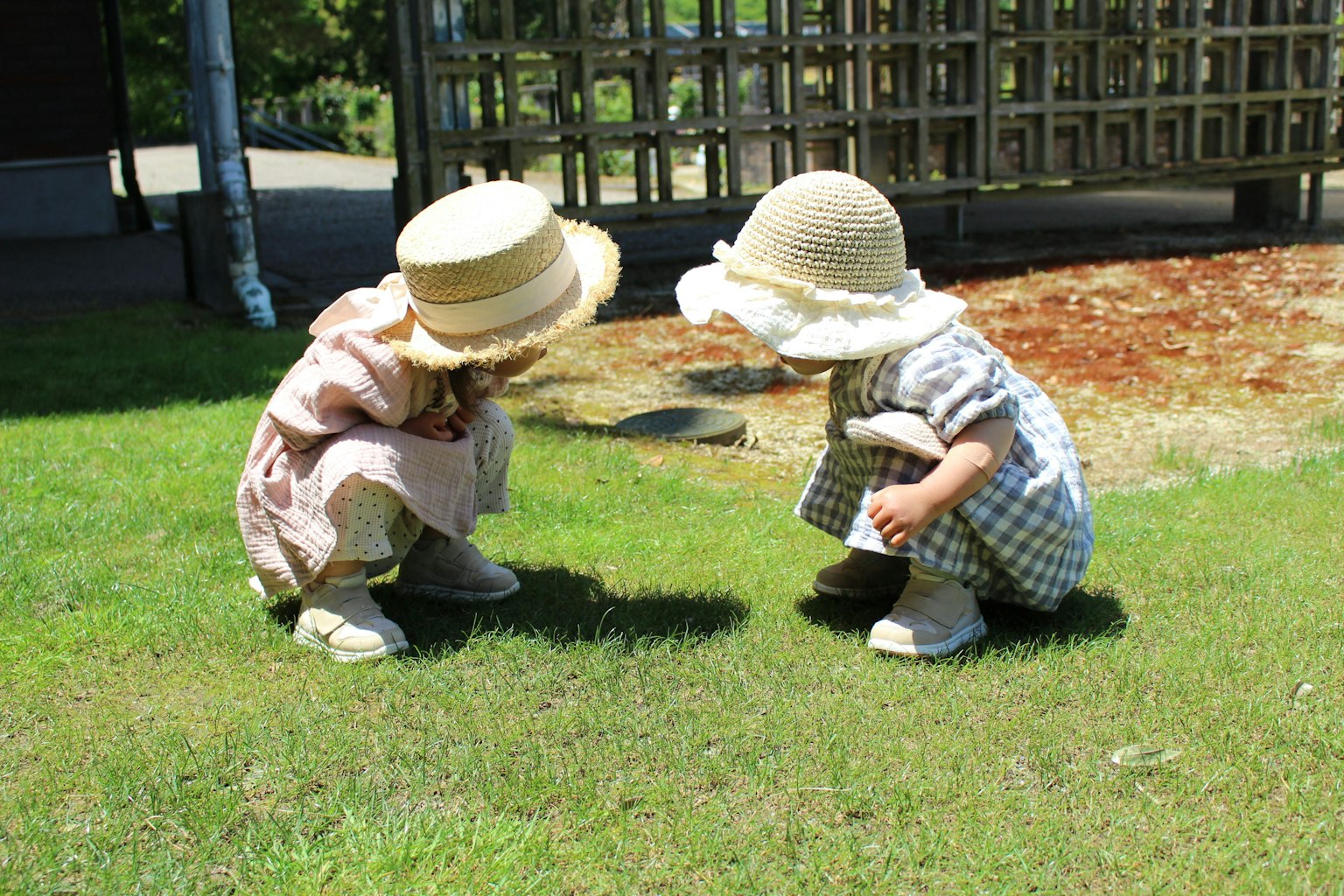 Zwei Kinder mit Hüten, die auf dem Gras hocken