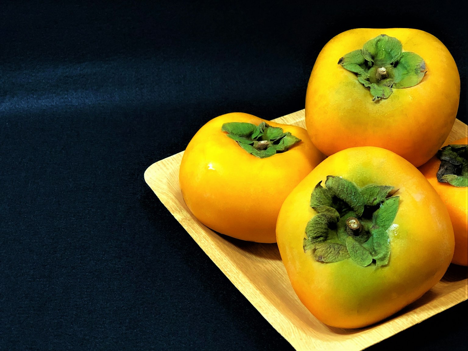 Una composizione di cachi dolci su un piatto di legno su sfondo nero