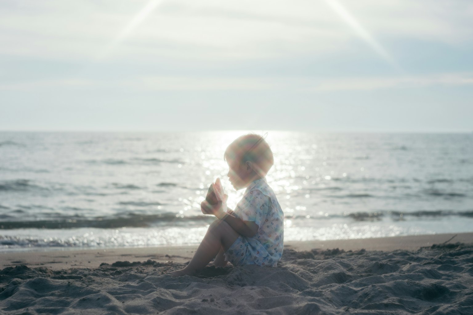 Silhouette di un bambino seduto tranquillamente sulla spiaggia con riflessi di luce