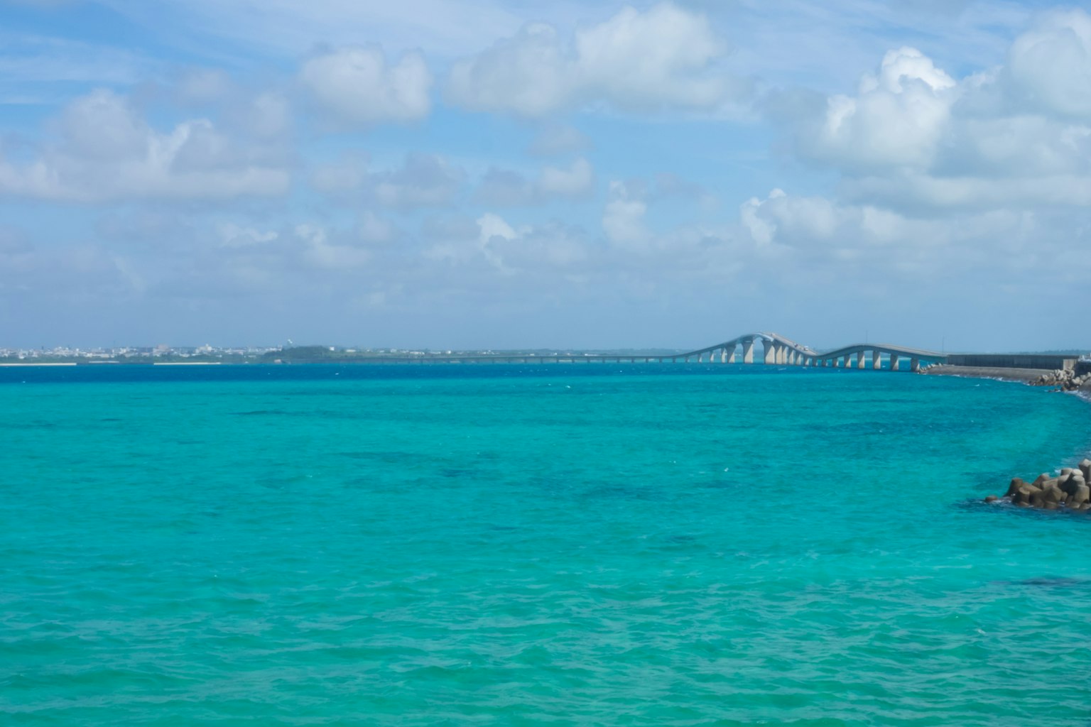 Laut turquoise cerah di bawah langit biru dengan awan berbulu