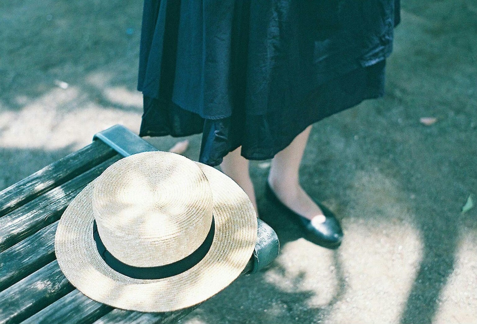 Ein Strohhut liegt neben den Füßen einer Frau in einem schwarzen Kleid