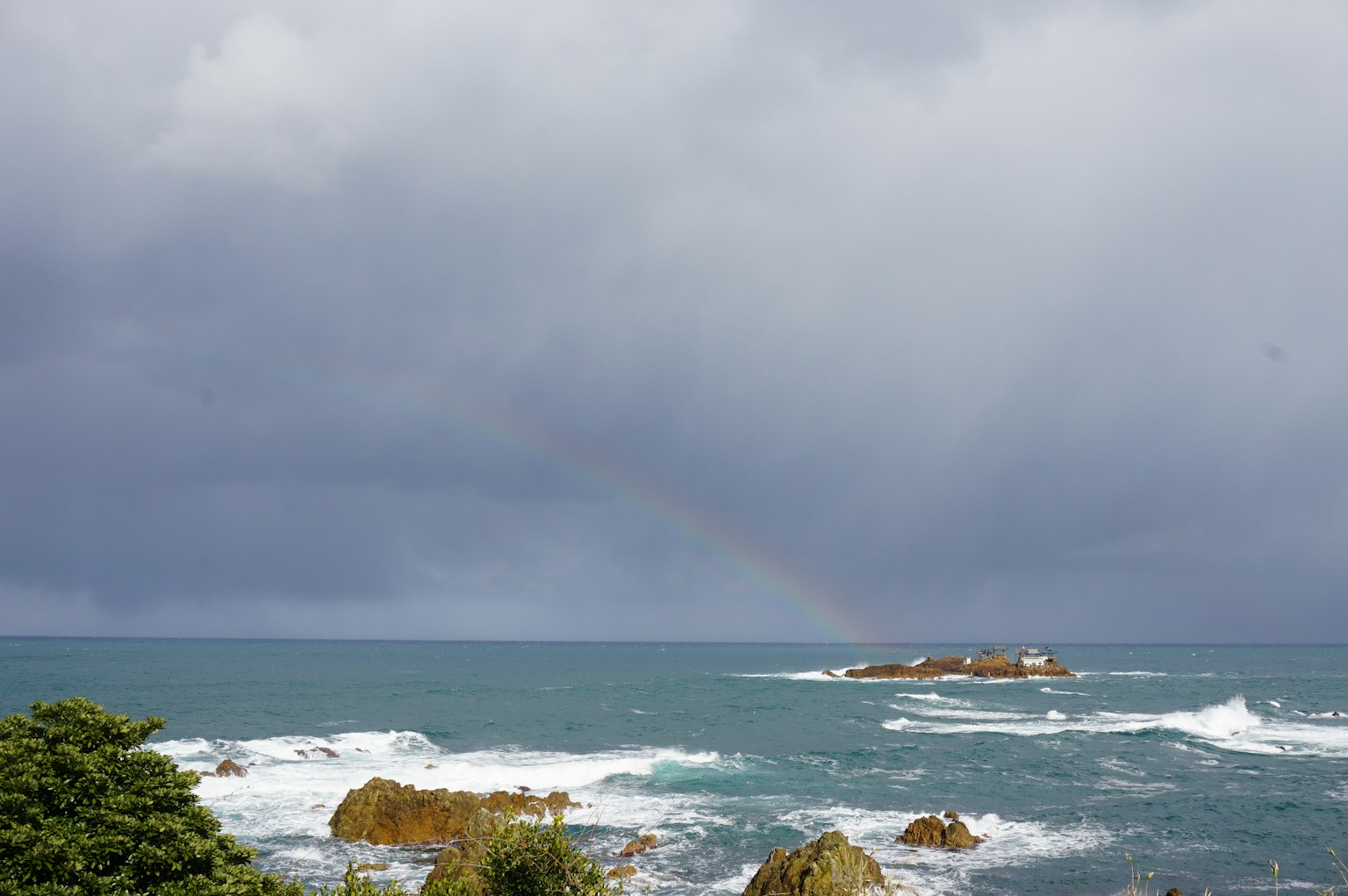 Waves crashing on the shore with a rainbow under dark clouds