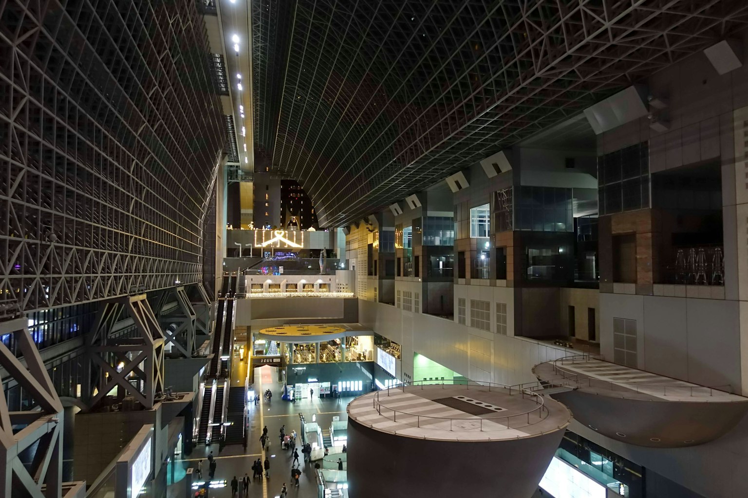 Vue intérieure d'un bâtiment moderne la nuit avec de hauts plafonds et un espace spacieux avec des zones commerciales illuminées