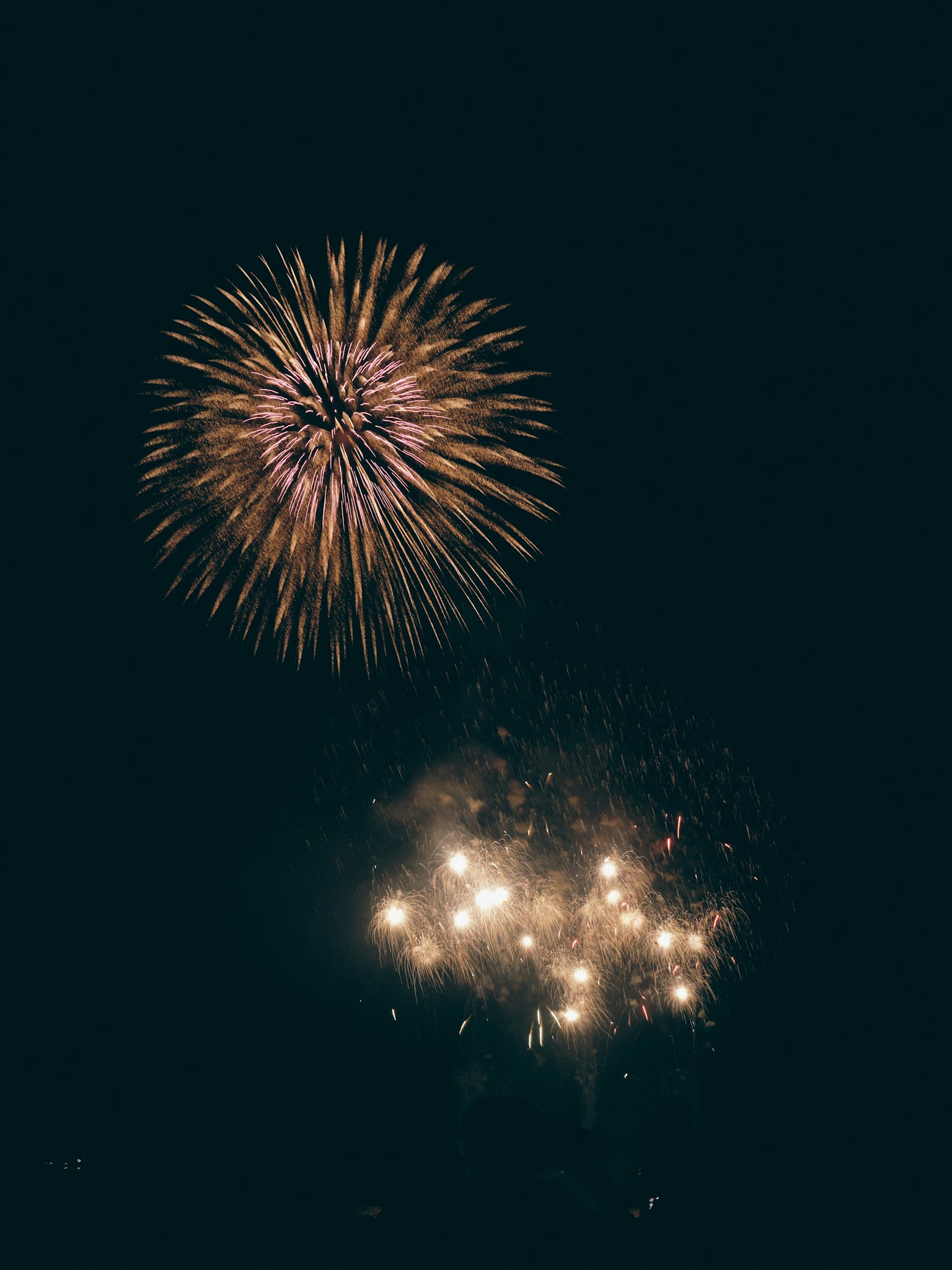 Colorful fireworks display in the night sky with a large firework on top and a cluster of smaller fireworks below