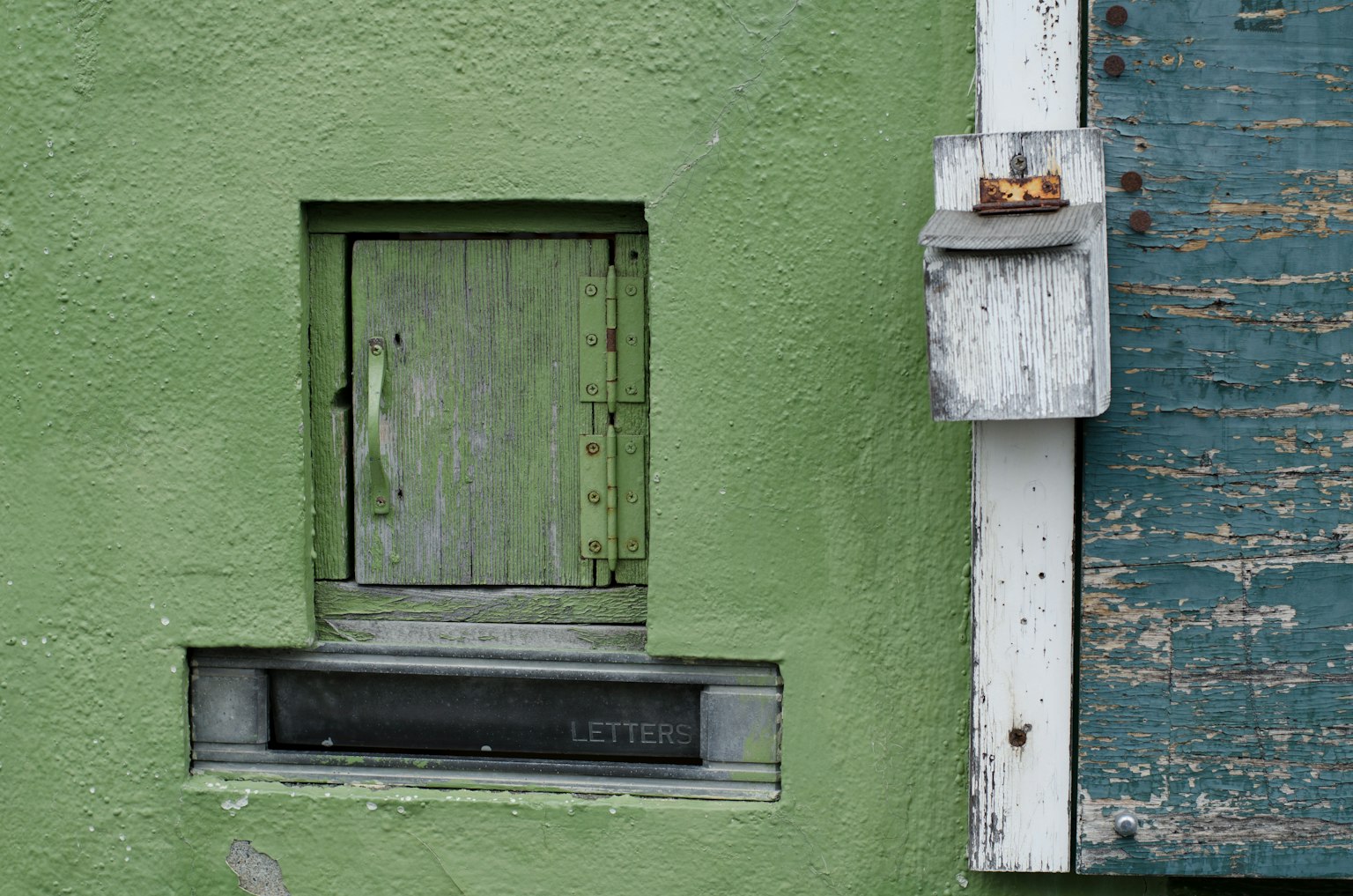 Kleine Holzfenster und Briefkasten an einer grünen Wand