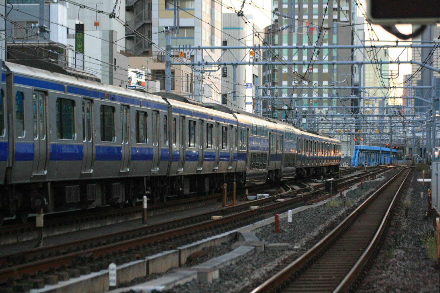 รถไฟสีเงินที่มีแถบสีน้ำเงินวิ่งไปตามฉากหลังของเมือง