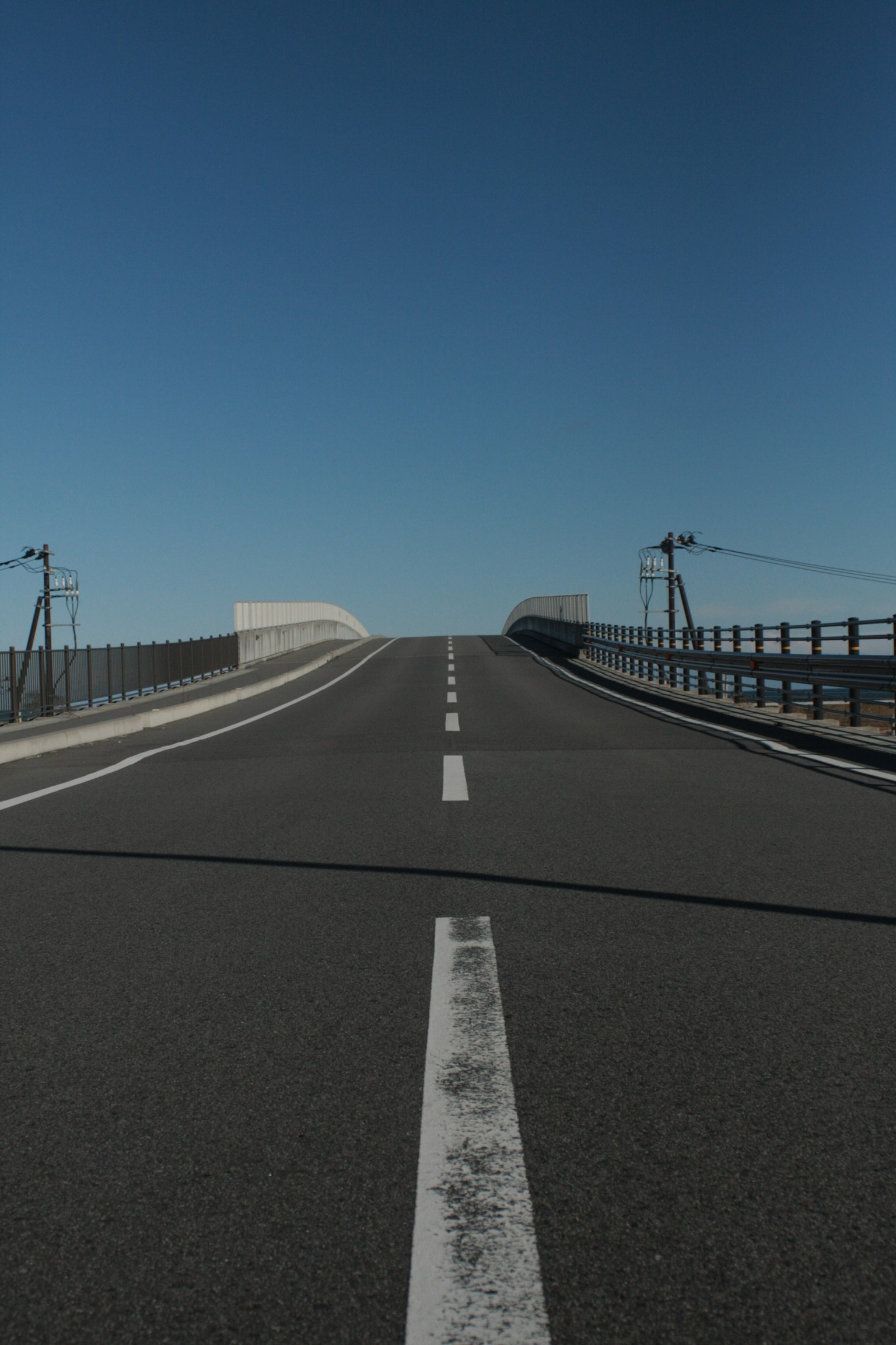 Ascending paved road under a blue sky with a white center line