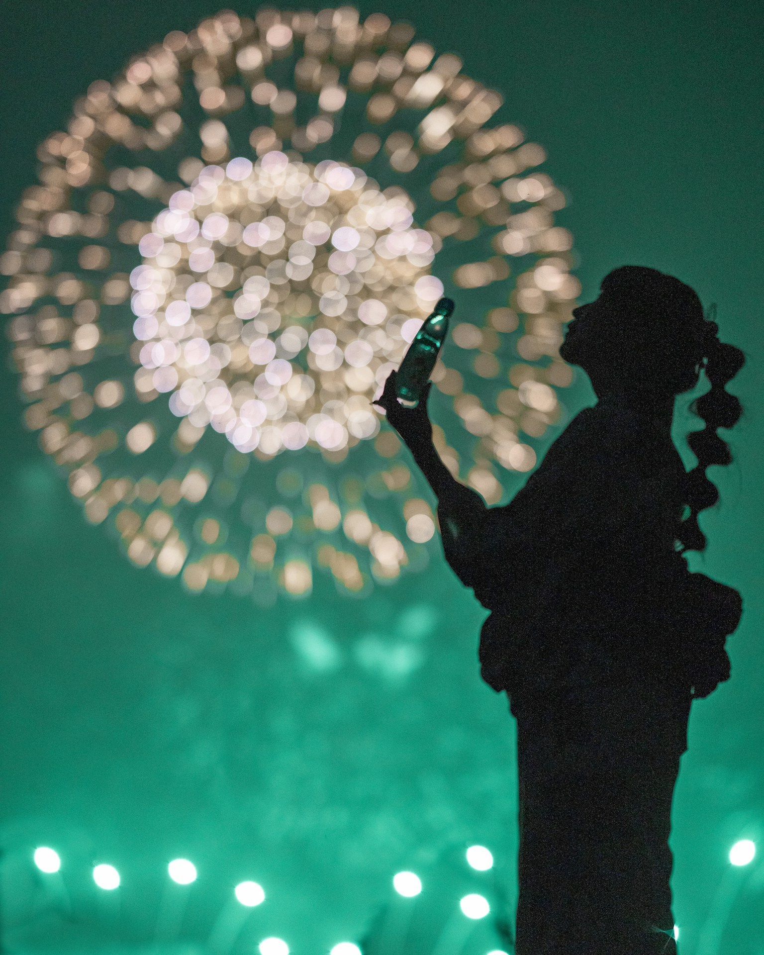 Silhouette of a woman in a kimono against a backdrop of fireworks in the night sky