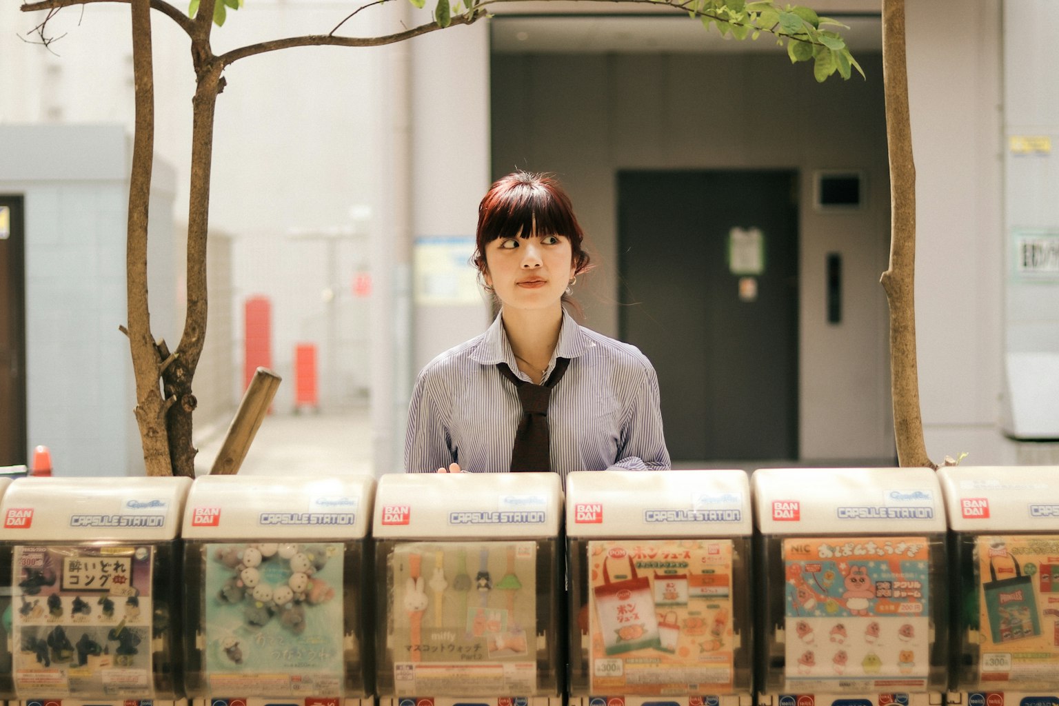 A woman standing in front of vending machines with buildings and trees in the background