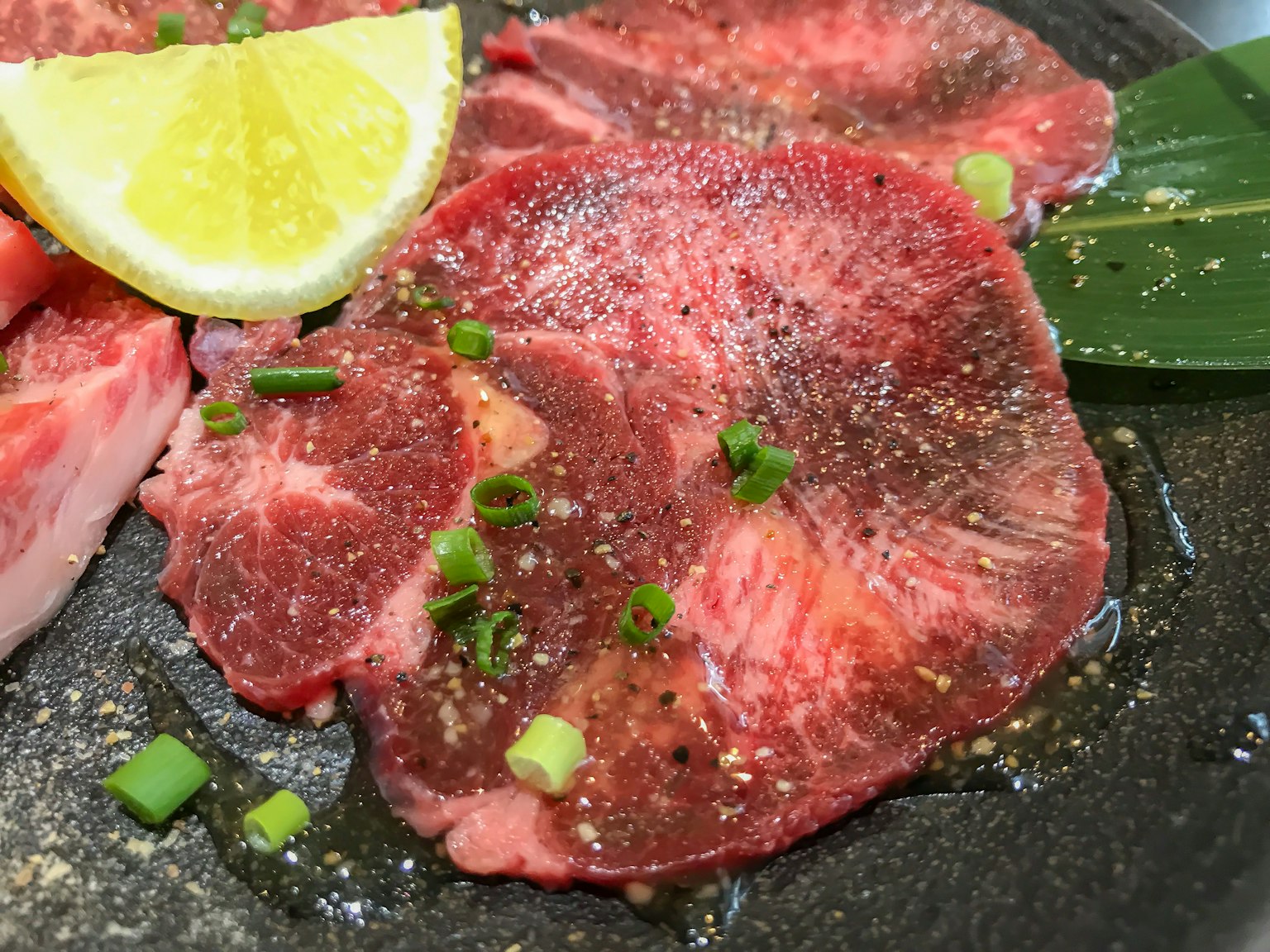 Carne en rodajas finas adornada con limón y cebollitas verdes