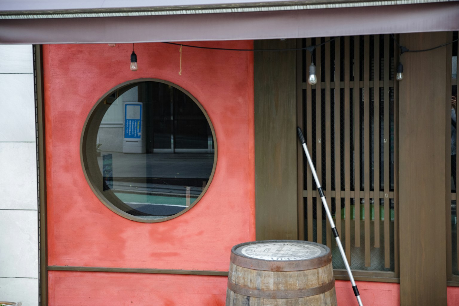 Exterior con una ventana redonda en una pared roja y un barril de madera