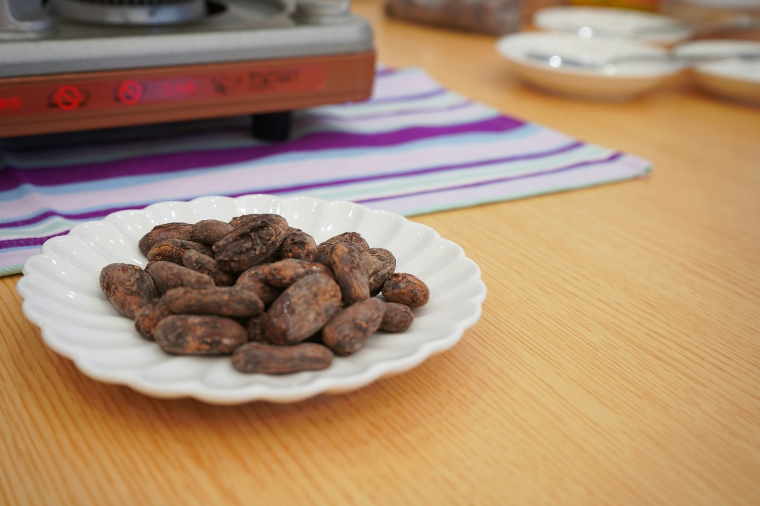 Une assiette de fèves de cacao sur une table en bois avec un réchaud en arrière-plan