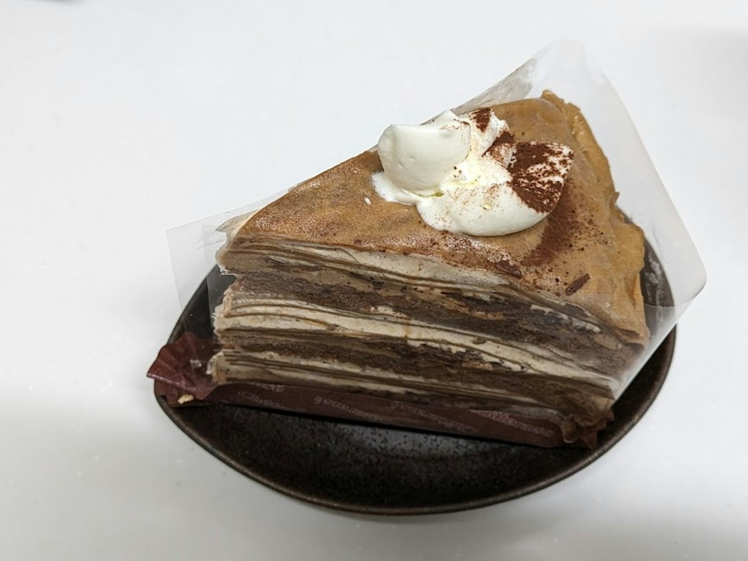 초콜릿 크레이프 케이크가 접시에 담겨 있고 휘핑 크림이 얹혀 있다