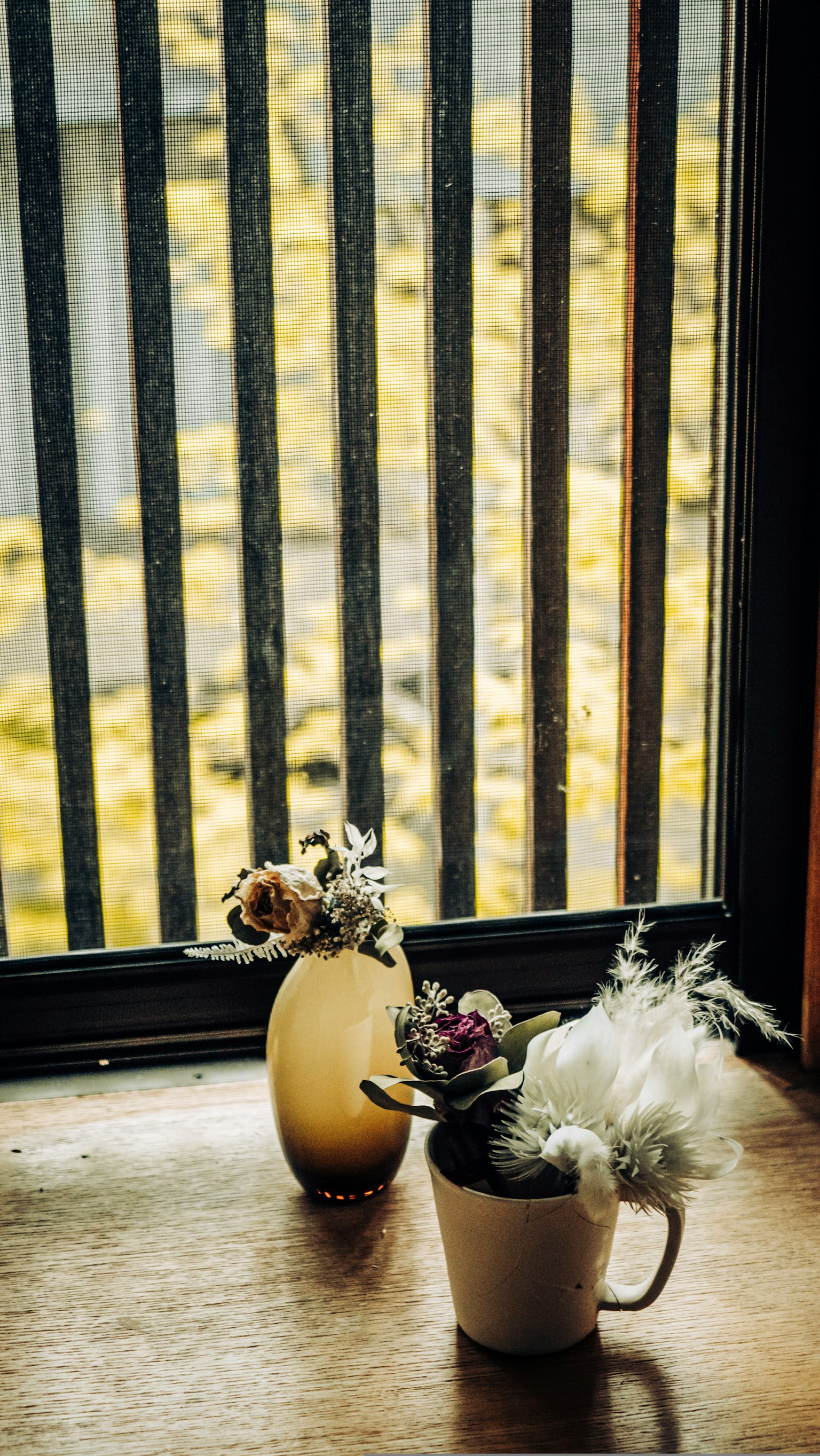 Arreglo de flores en un jarrón y una taza en el alféizar de una ventana