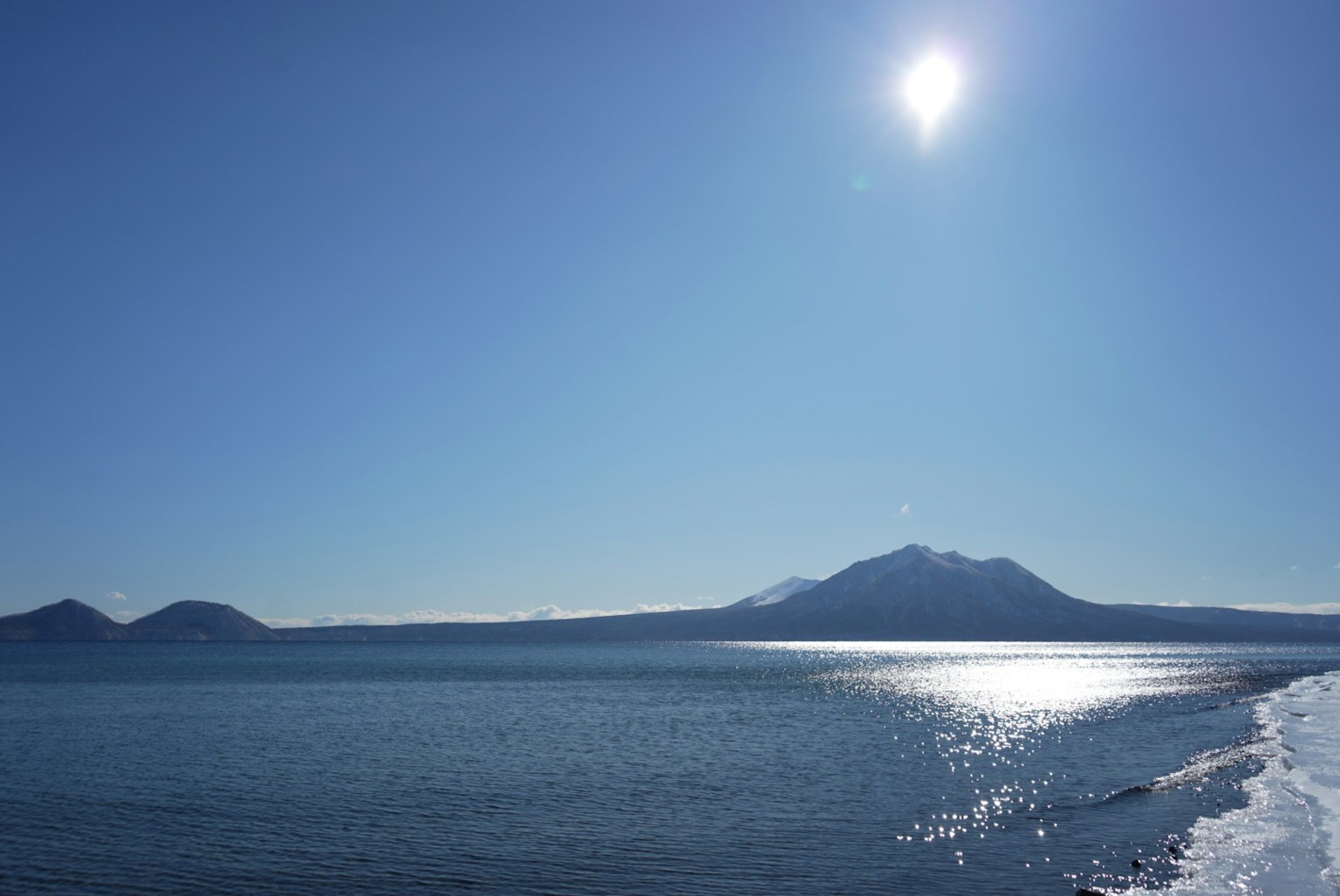 Pemandangan langit biru cerah dan laut, matahari bersinar terang, gunung di kejauhan