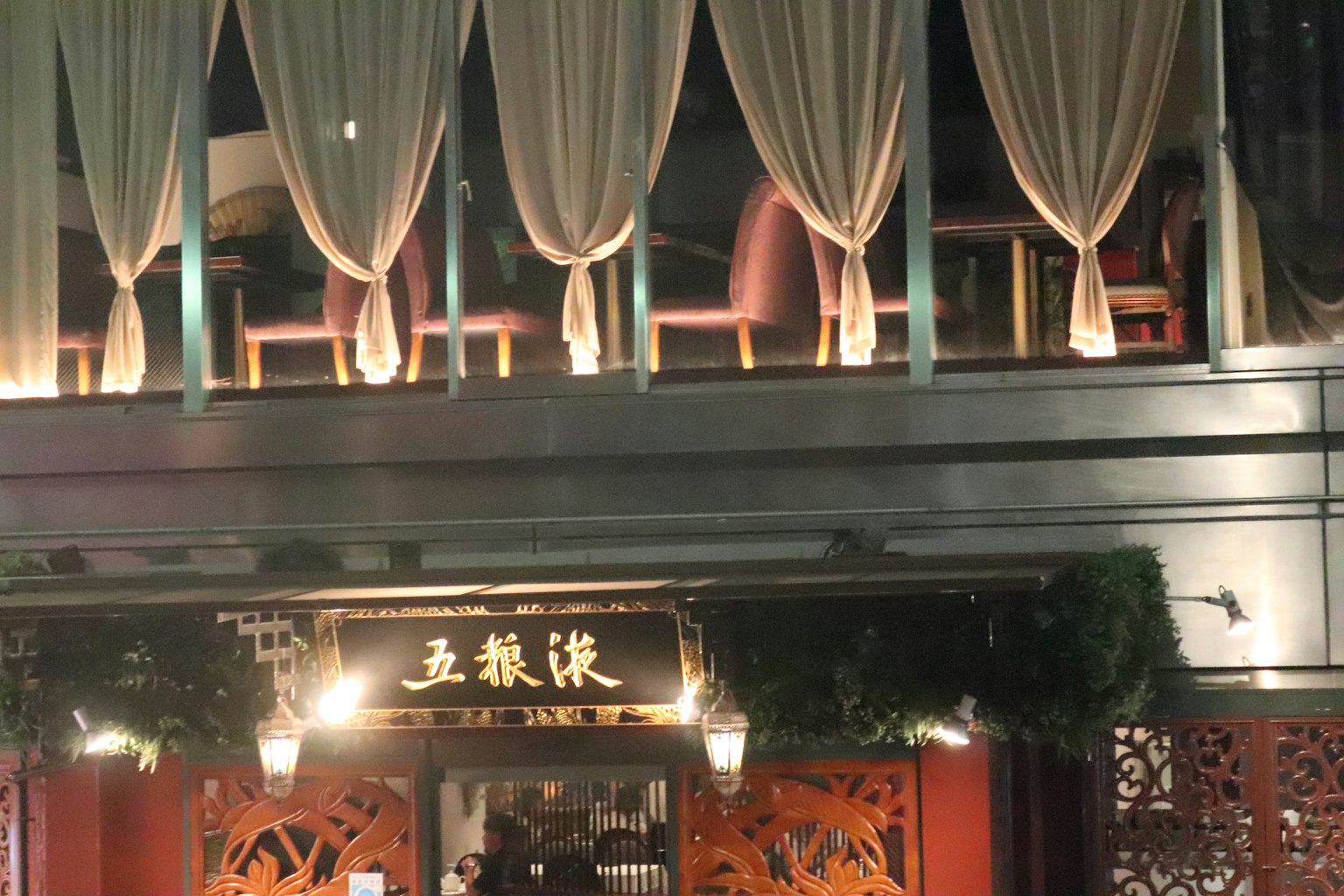 Facciata del ristorante illuminata di notte con tende drappeggiate e sedie visibili