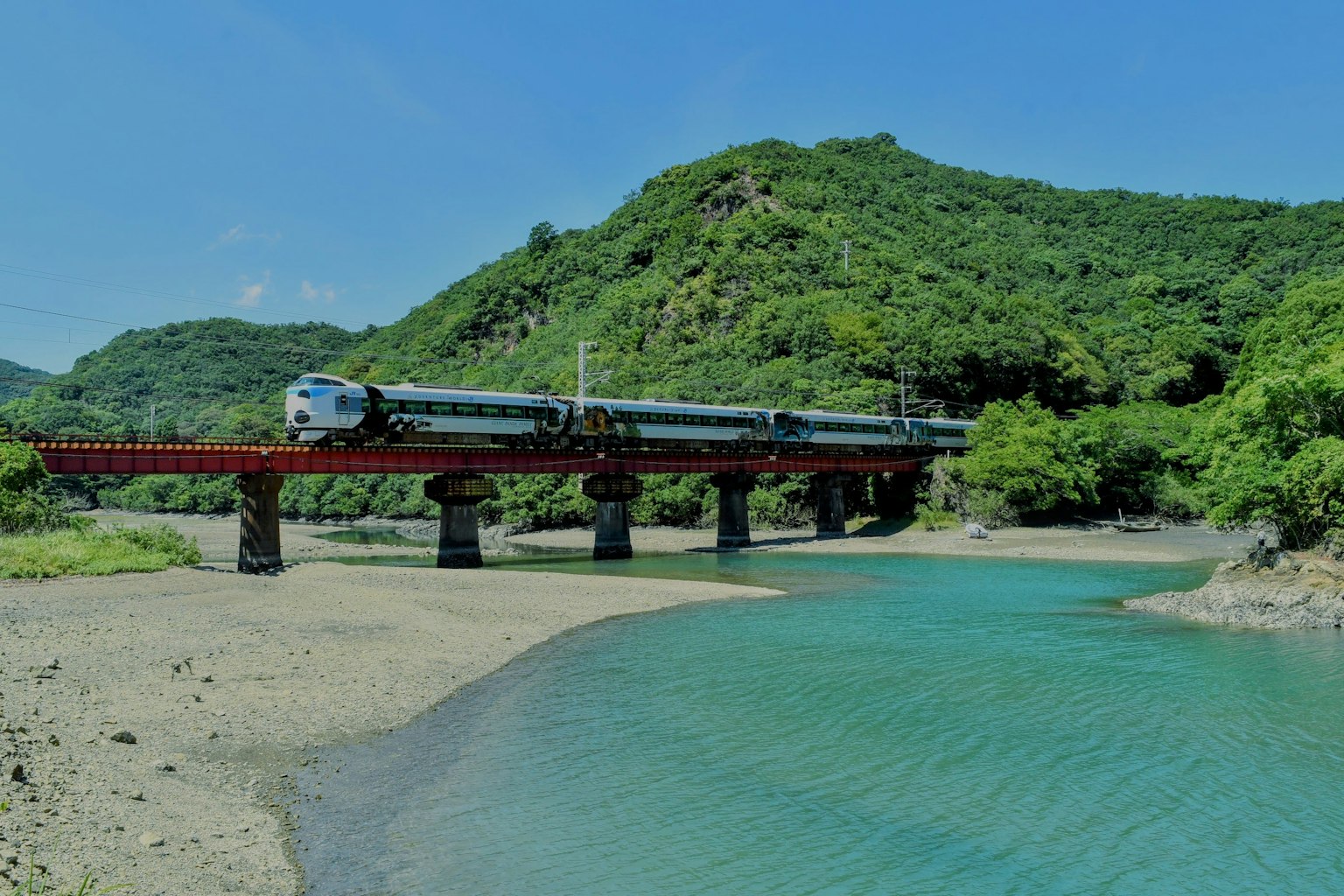 รถไฟข้ามสะพานที่ตั้งอยู่ท่ามกลางภูเขาที่เขียวชอุ่มและแม่น้ำ