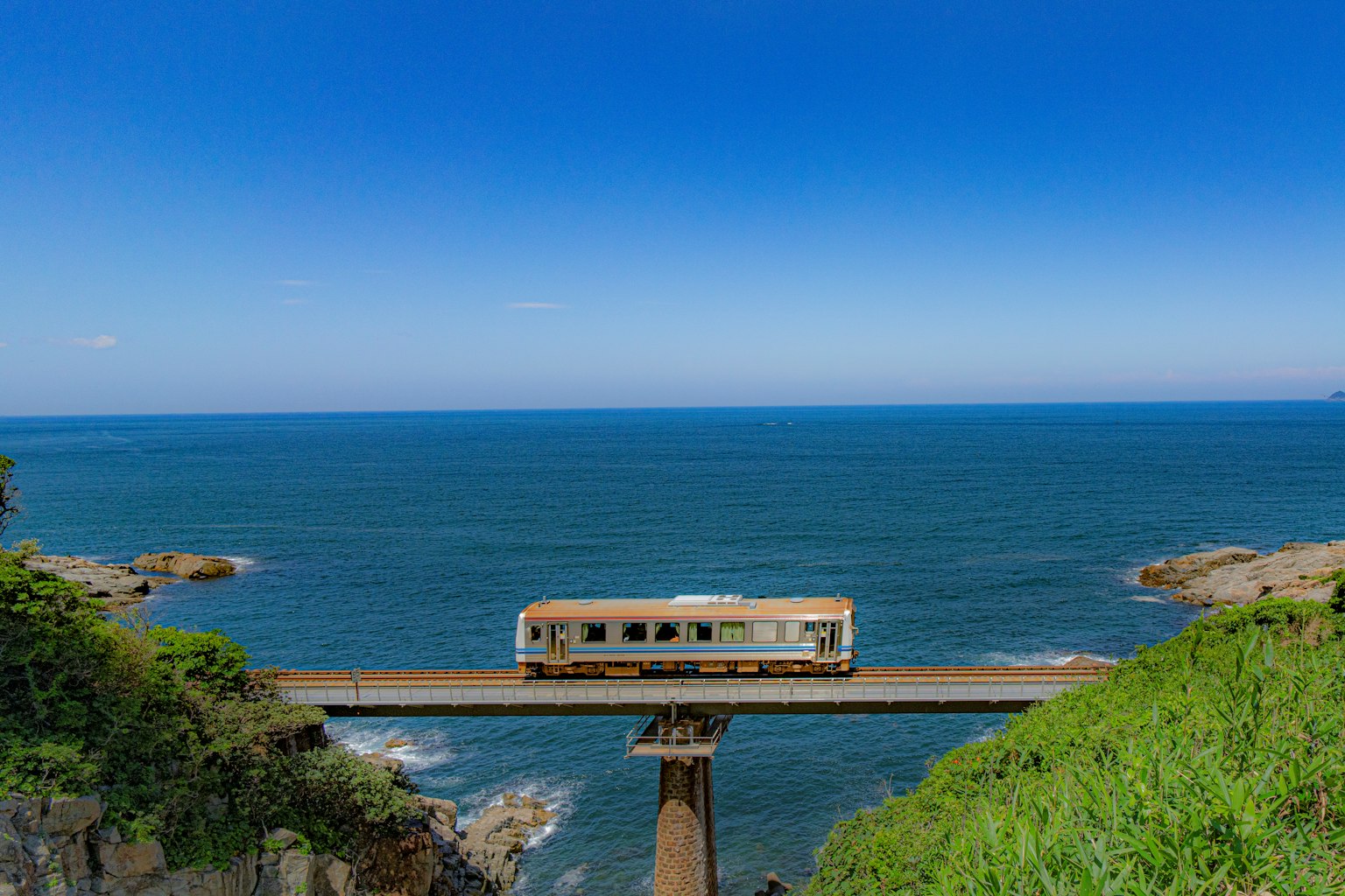 Tren cruzando un puente sobre el mar azul con cielos despejados