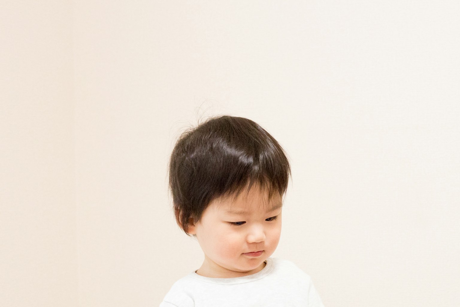 Seorang anak kecil tersenyum sambil melihat ke bawah di latar belakang putih
