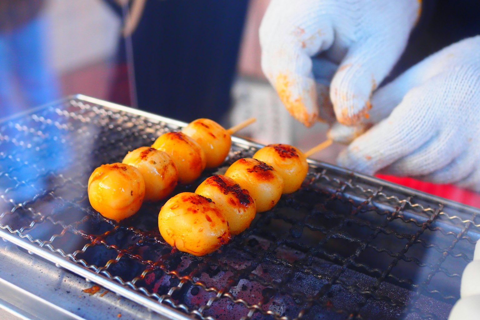 Hands grilling skewered dango on a grill