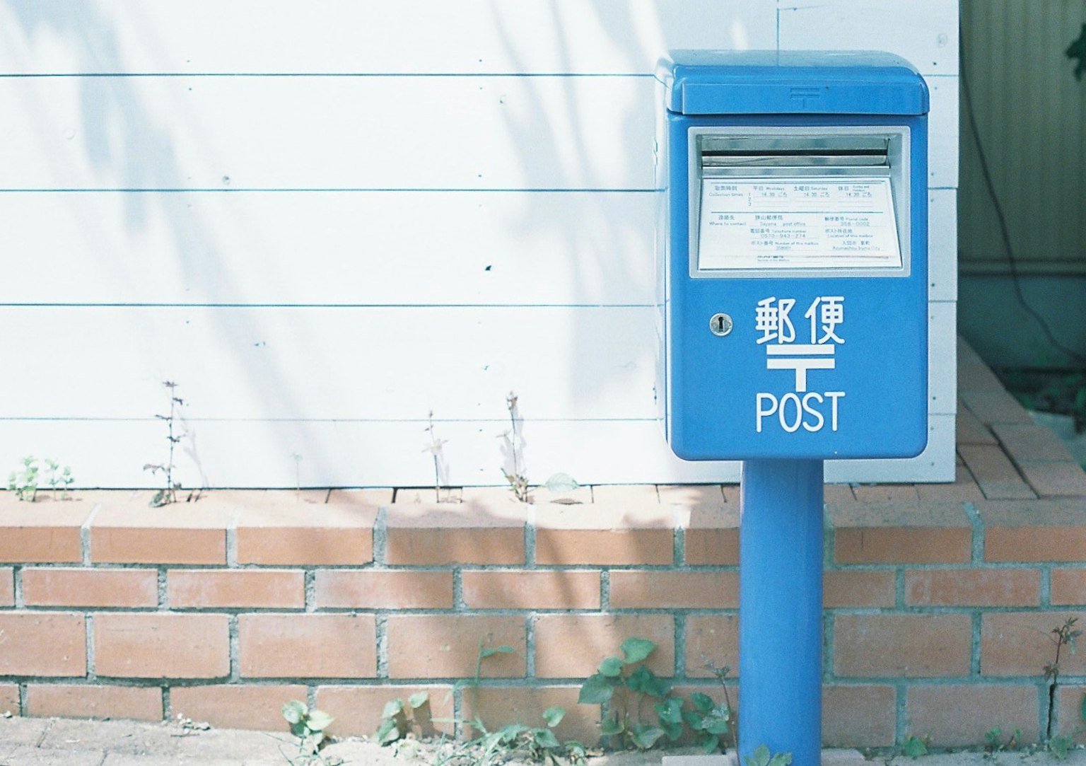 A blue mailbox stands in front of a white wall