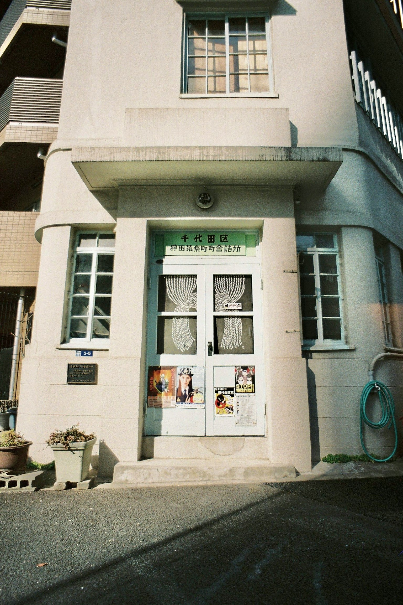 Vista frontal de un edificio antiguo con una puerta blanca y un letrero verde
