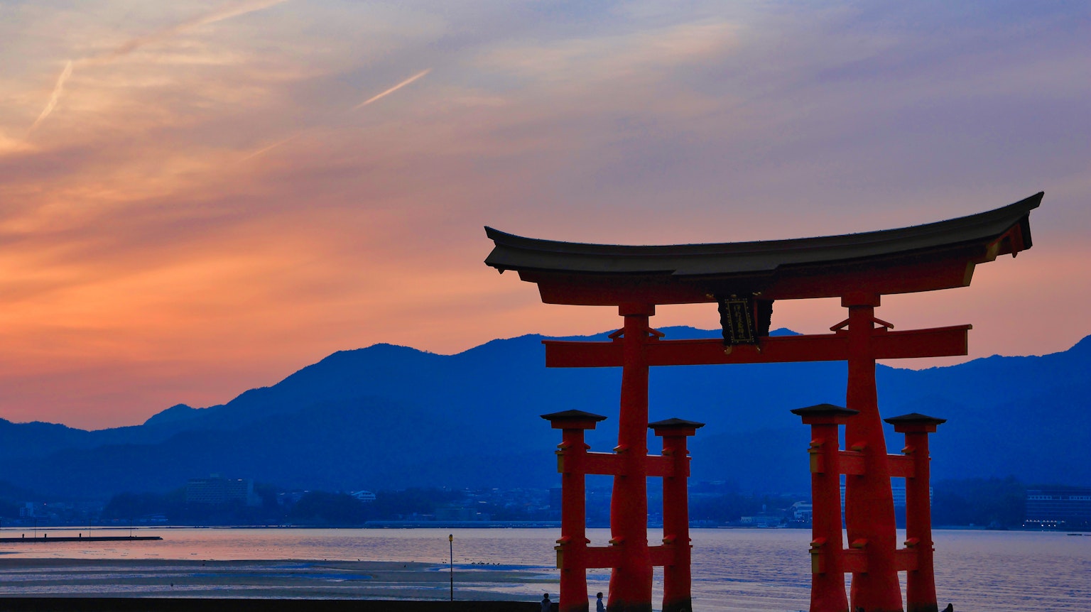 Silhouette of a red torii gate against a sunset and mountains